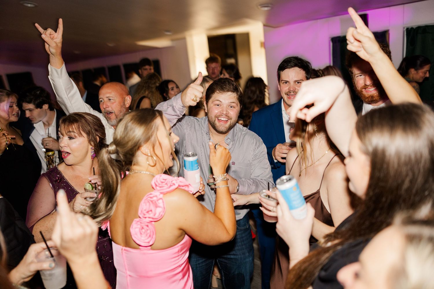 Energetic crowd dancing and celebrating at a reception with purple ambient lighting.