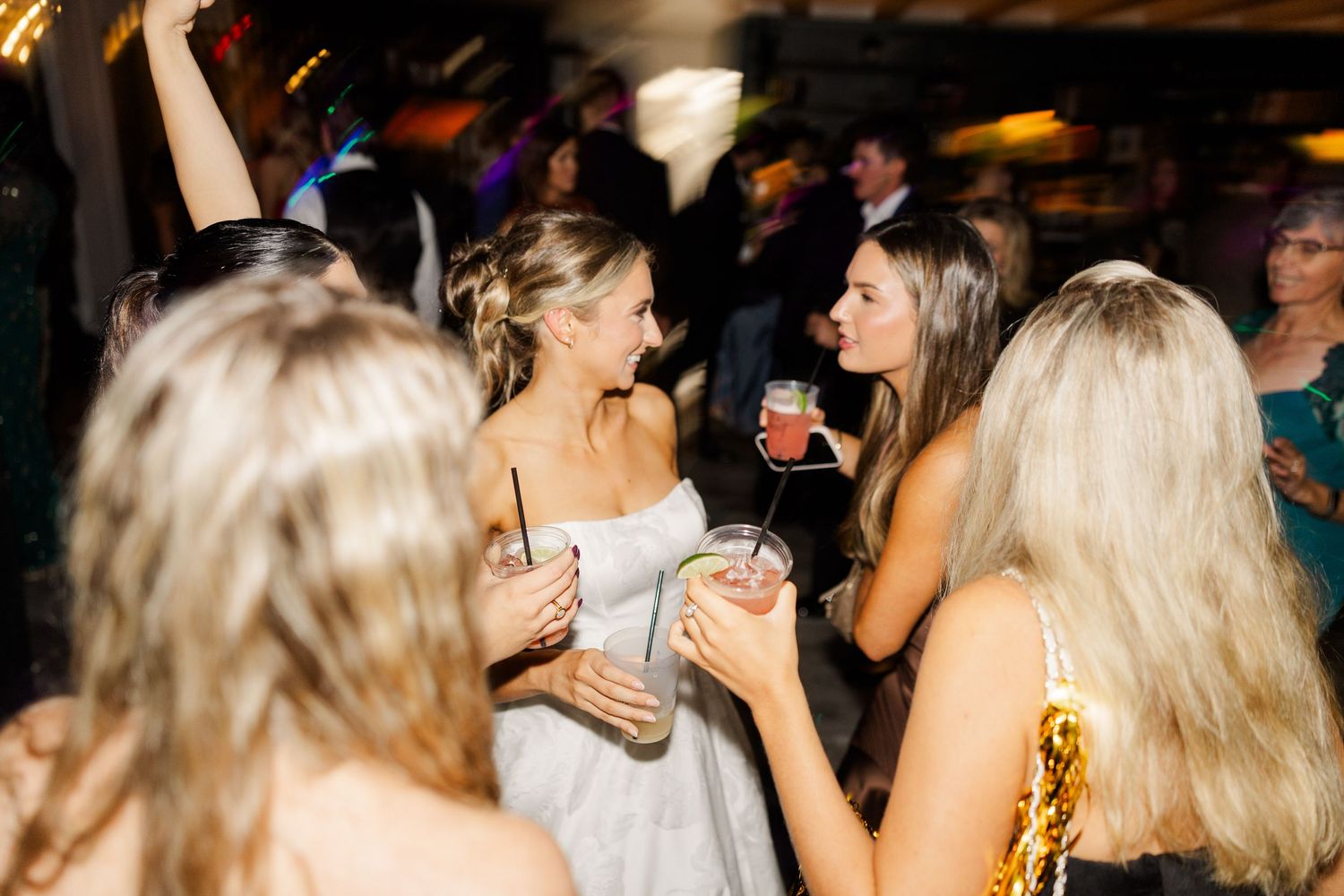 Wedding reception guests dancing and celebrating on a dimly lit dance floor with warm lighting.