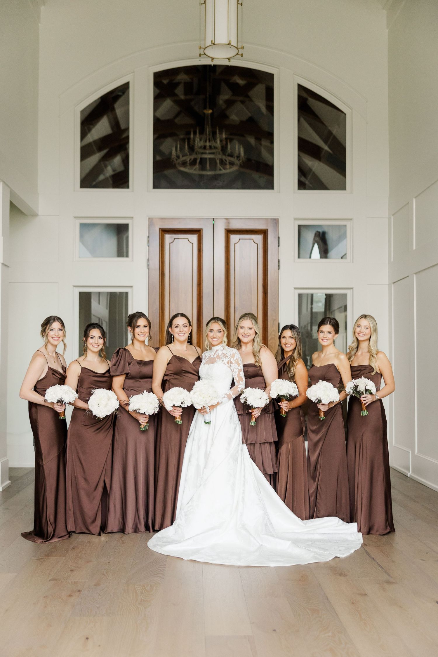 Wedding party photo with bridesmaids in brown dresses posing with bride in white gown.