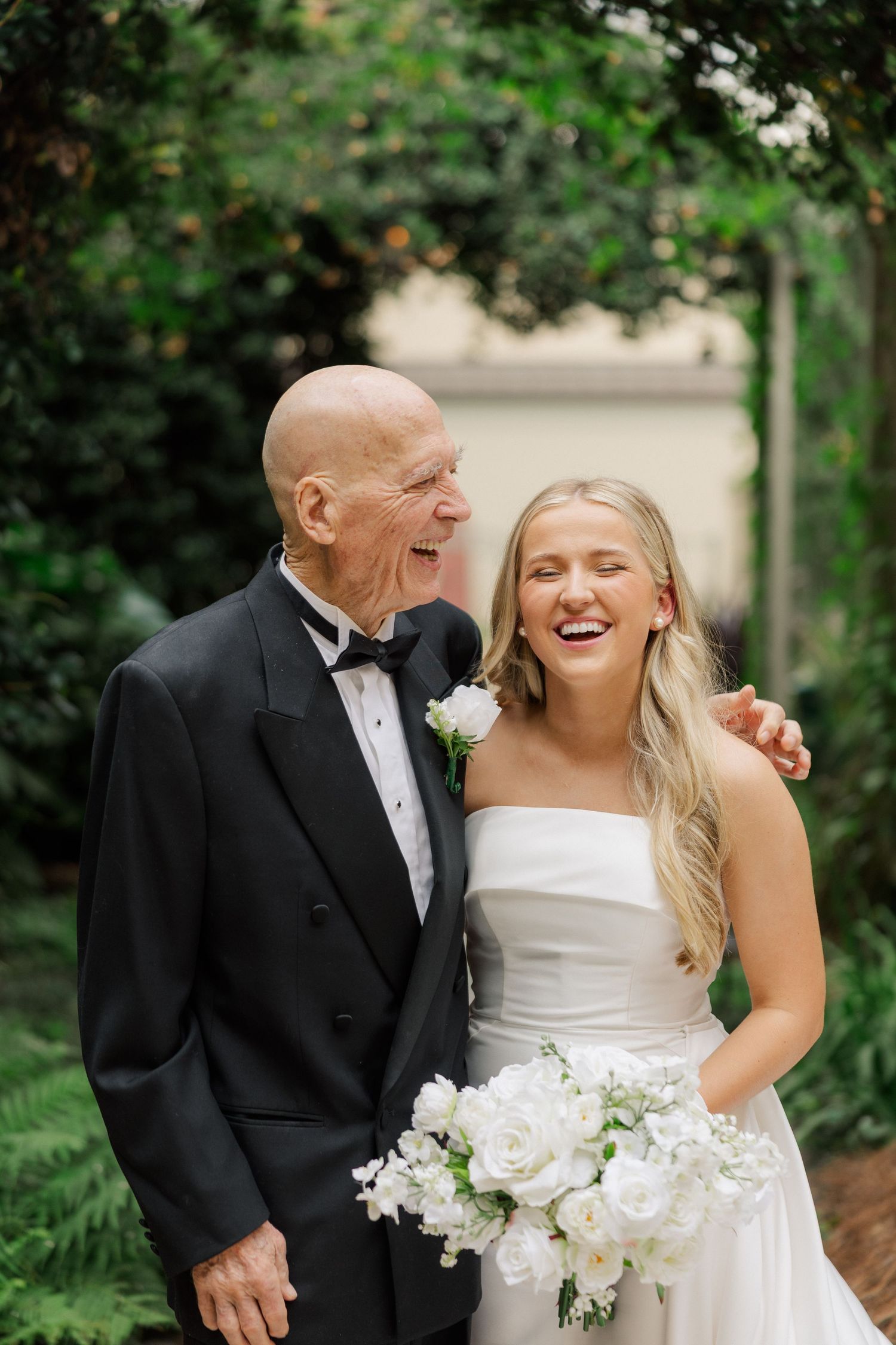 A joyful moment captured between a bride in white and an older gentleman in formal attire outdoors.