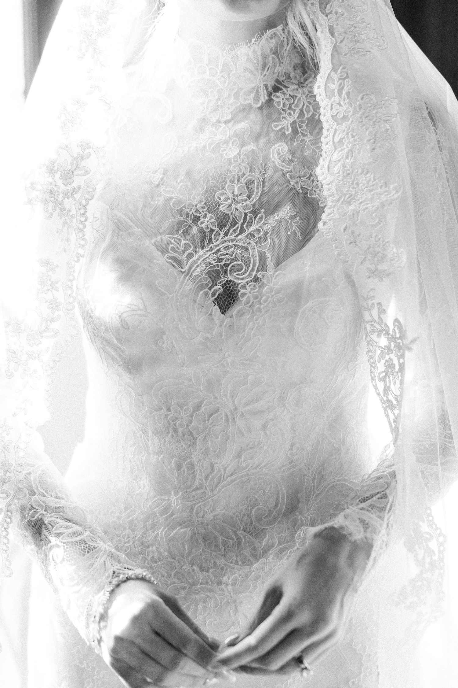 Close-up black and white detail of intricate lace wedding dress bodice with delicate floral patterns.
