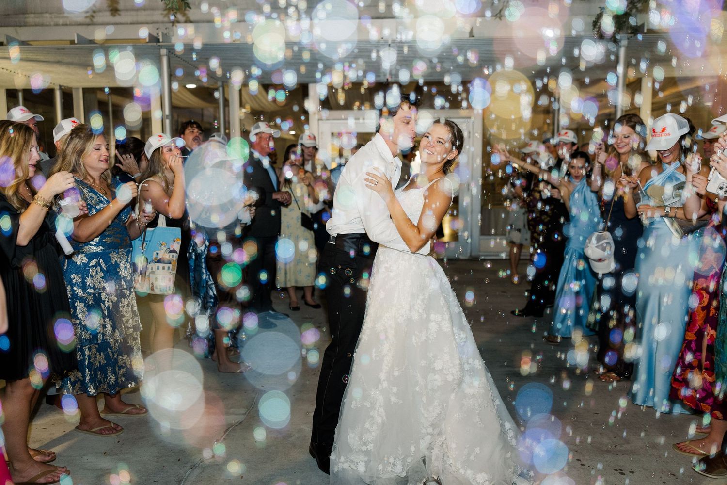 Wedding couple celebrates on dance floor surrounded by bubbles and party lighting effects.