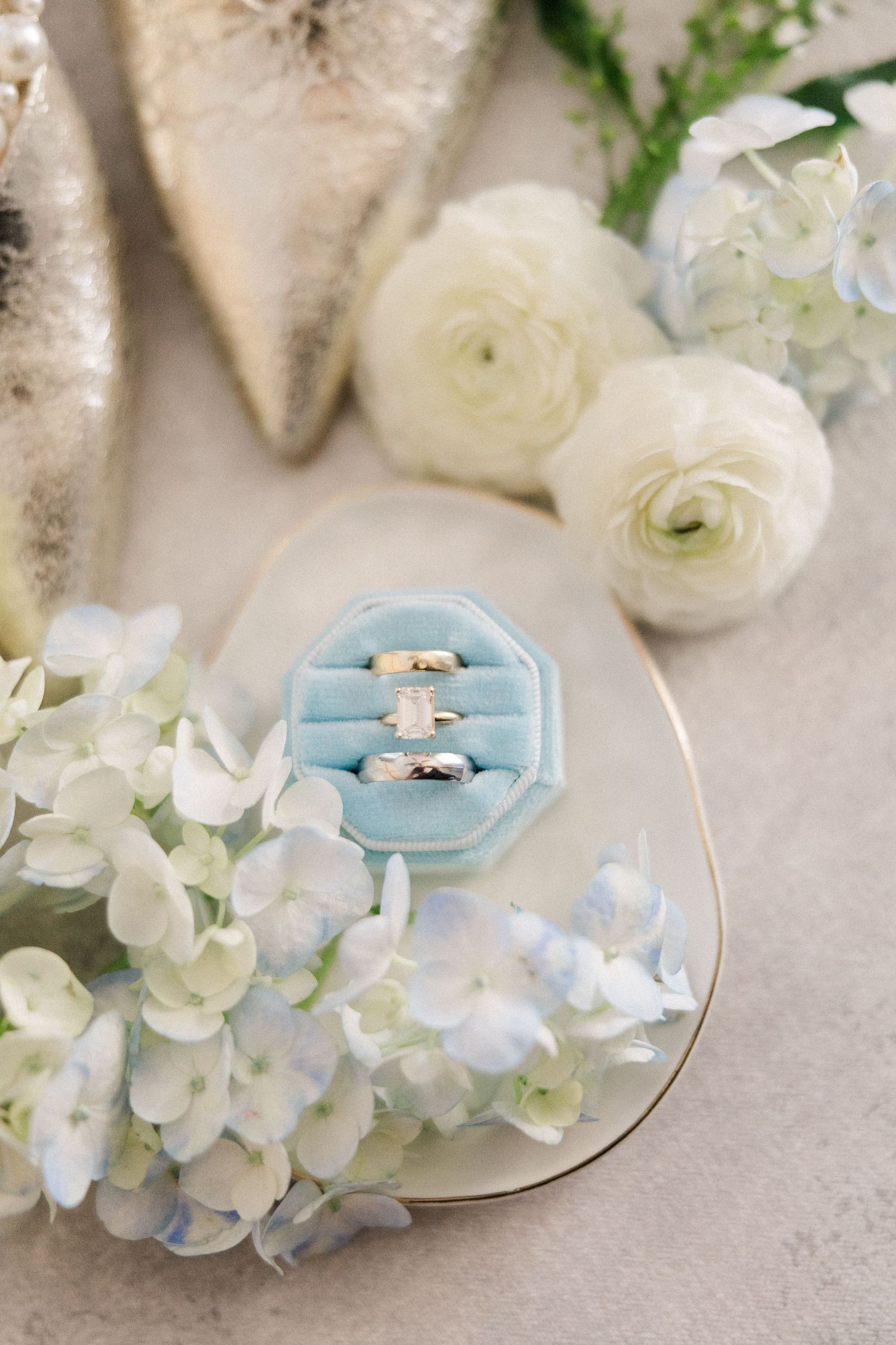 Wedding rings nestled in light blue ring boxes surrounded by delicate white hydrangeas and flowers.
