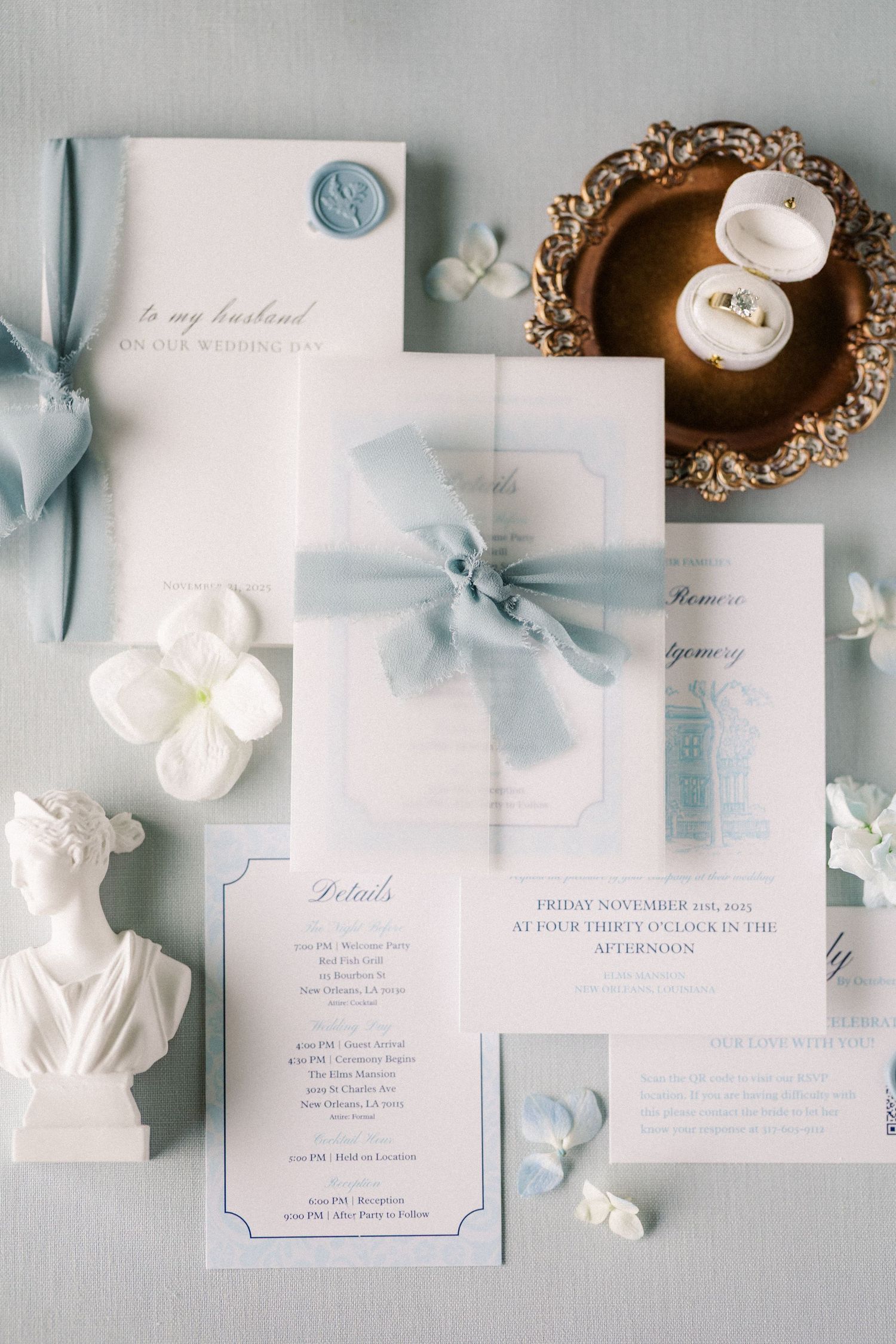 Elegant wedding stationery suite in soft blue and white with floral accents and delicate ribbons laid out on gray fabric.