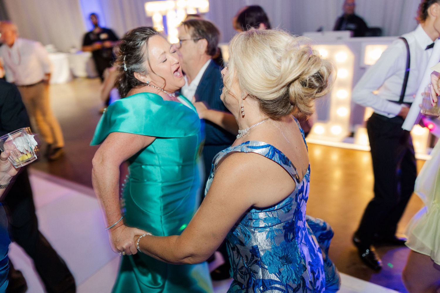 Wedding reception dance party with guests in vibrant blue and teal formal attire.