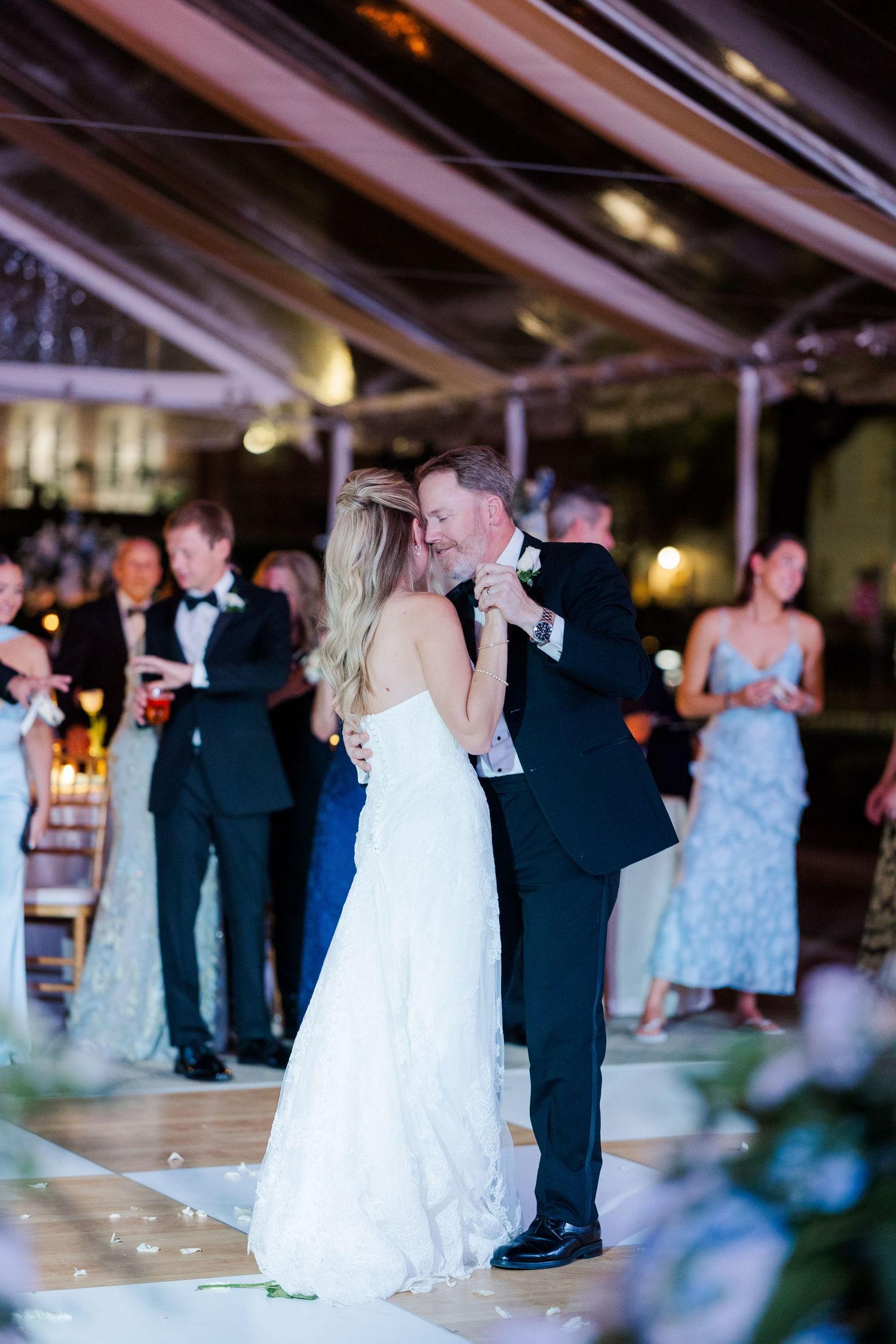 Wedding reception guests dancing on an illuminated dance floor under tent lighting.