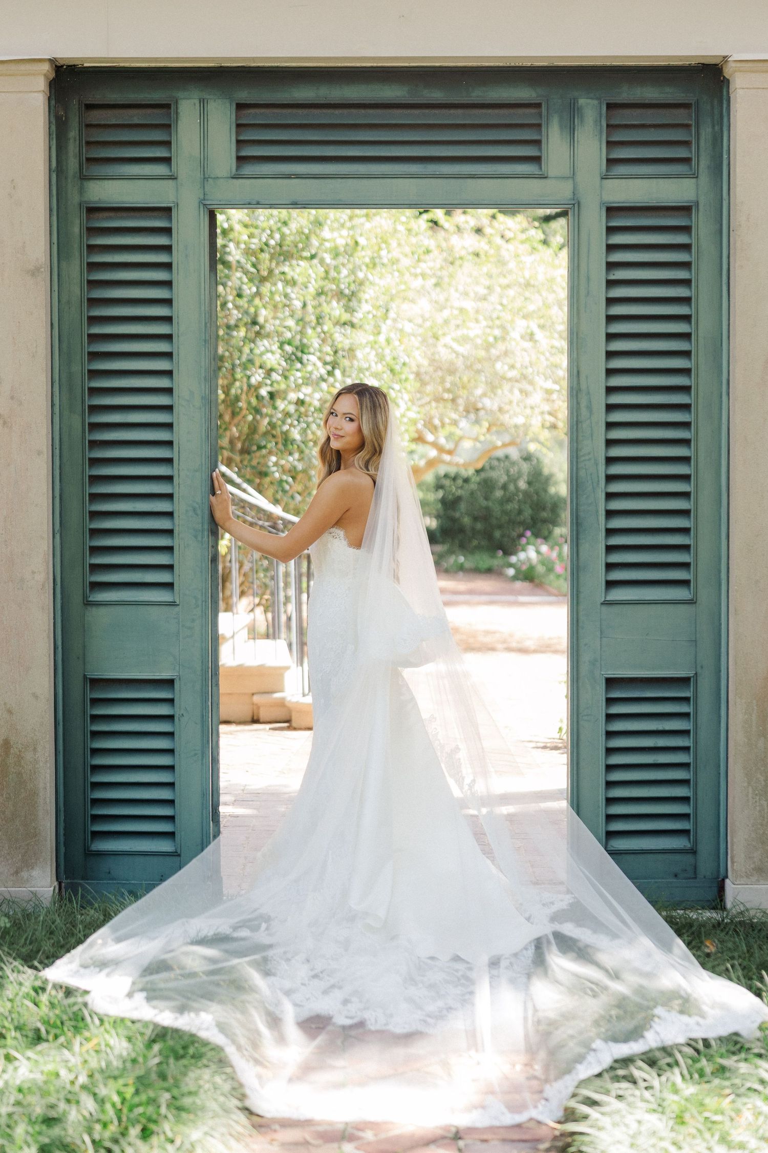Wedding dress train flows beautifully across a veranda with green plantation shutters.