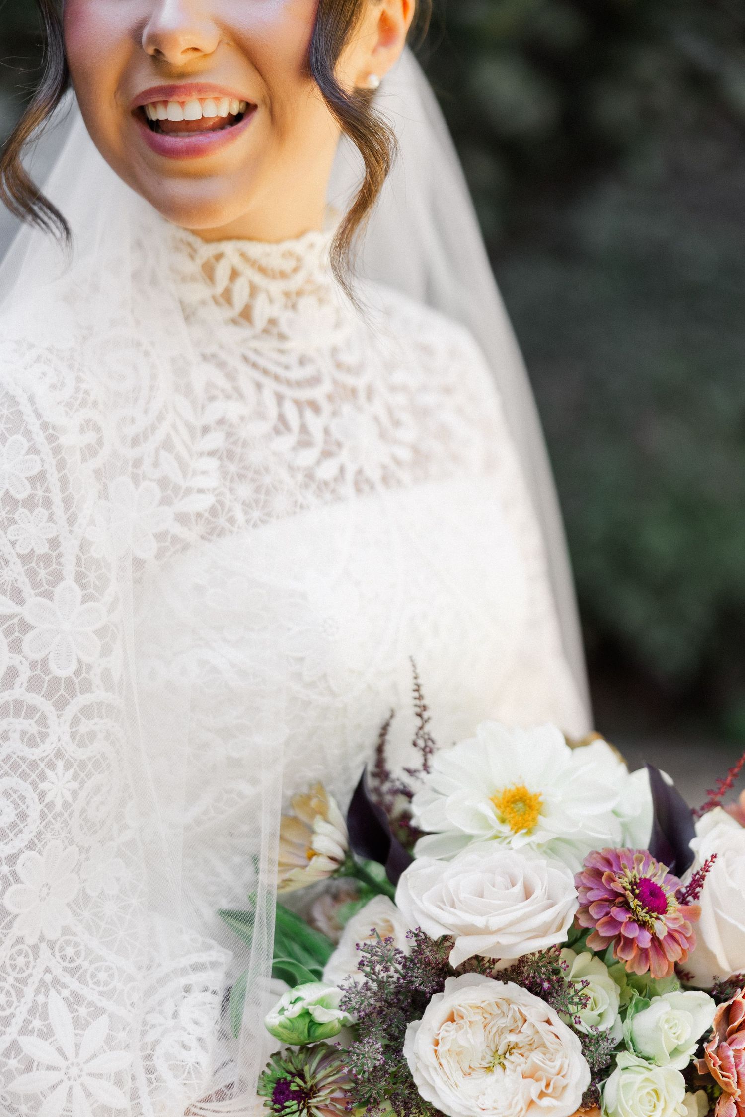A close-up detail of a bride's lace wedding dress and floral bouquet featuring roses and mixed flowers.