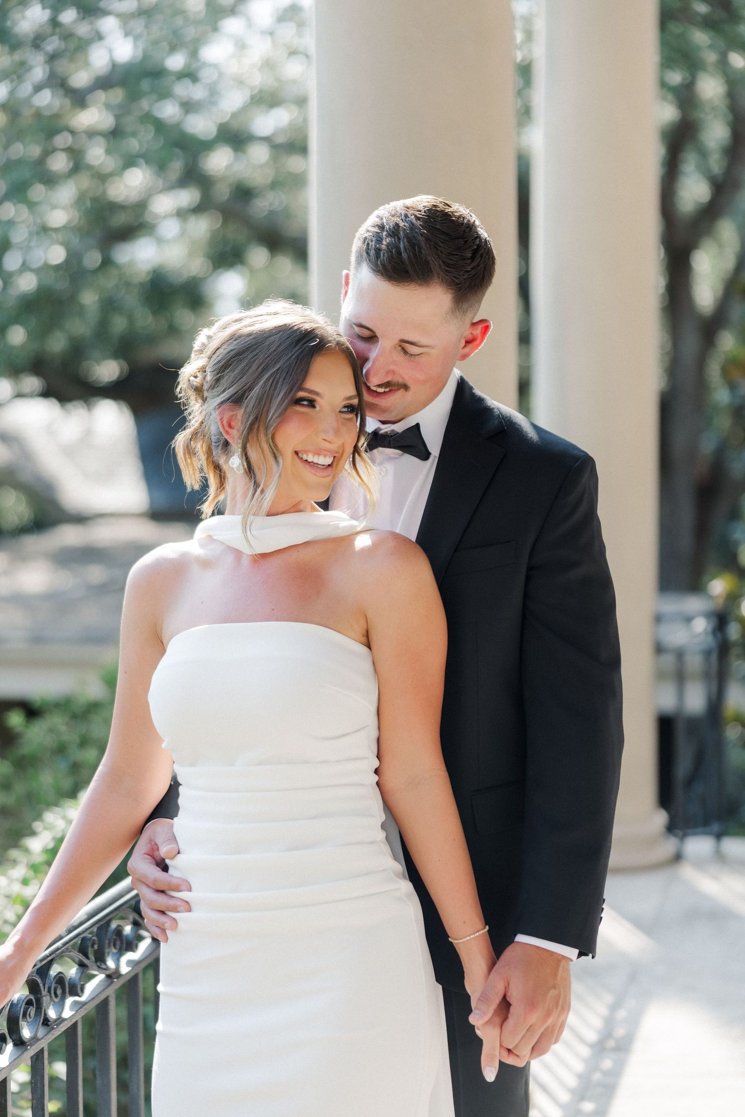 A tender wedding moment captured between a couple on a columned porch with soft natural lighting.