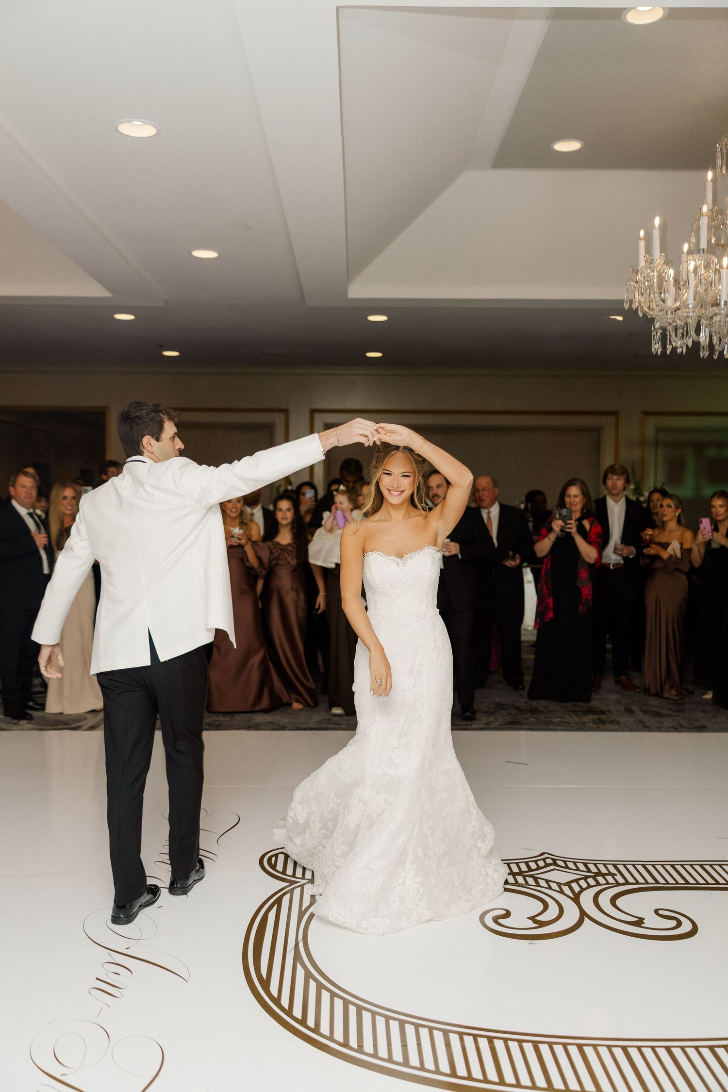 Wedding couple performs their first dance on a white floor with decorative pattern.