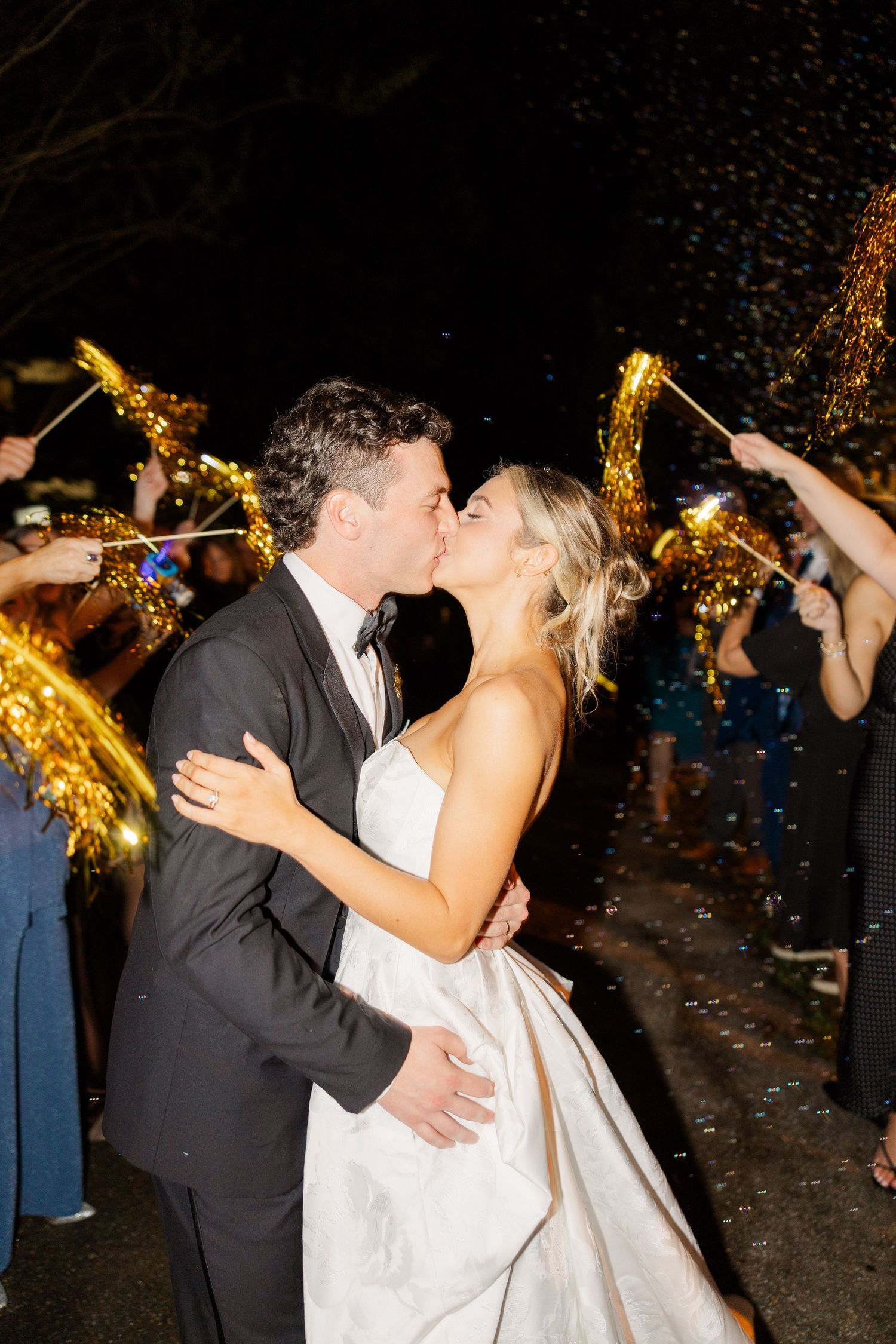 Newlyweds share romantic kiss during nighttime sparkler exit celebration.