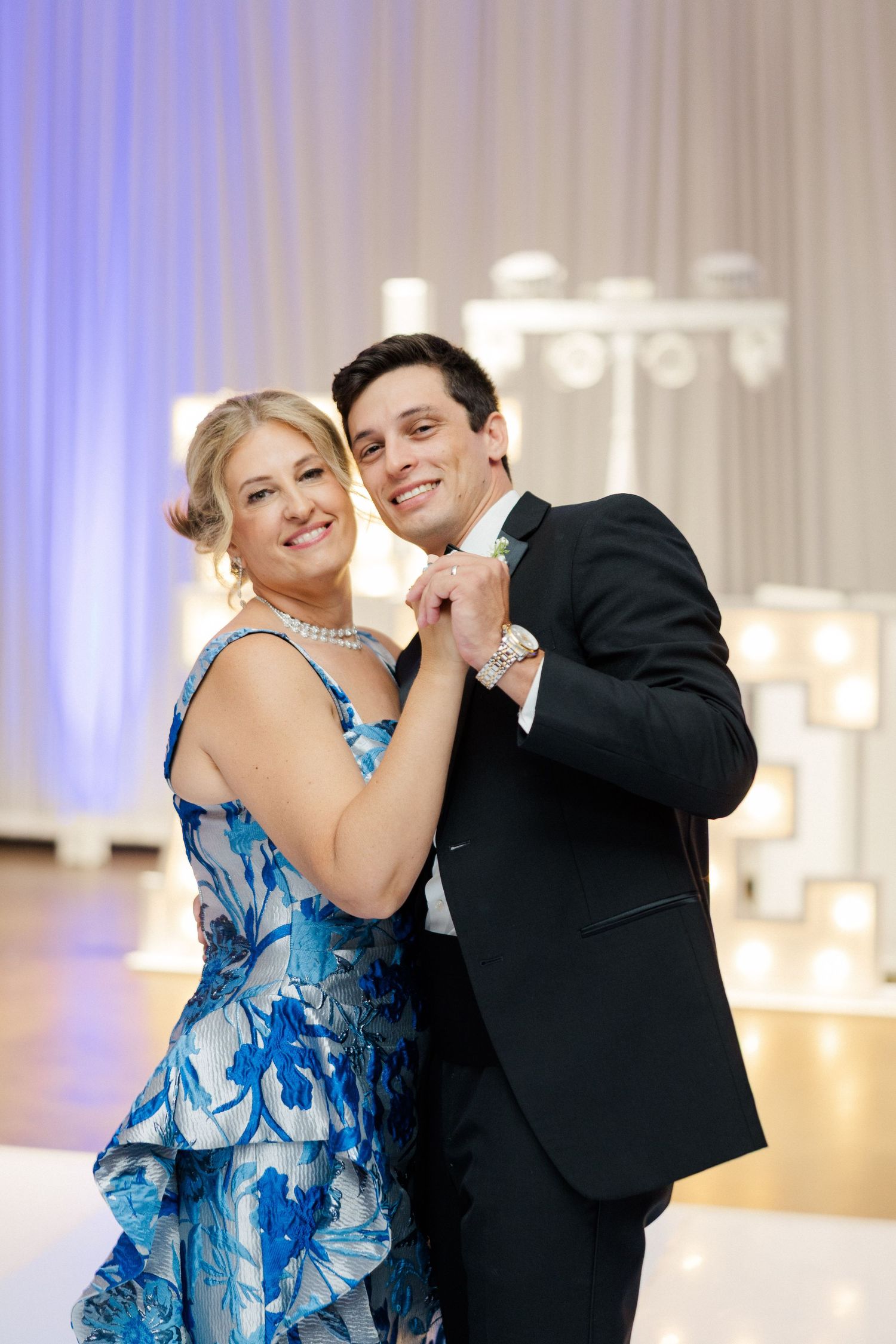 Wedding reception guests dance and celebrate in a ballroom with blue uplighting.