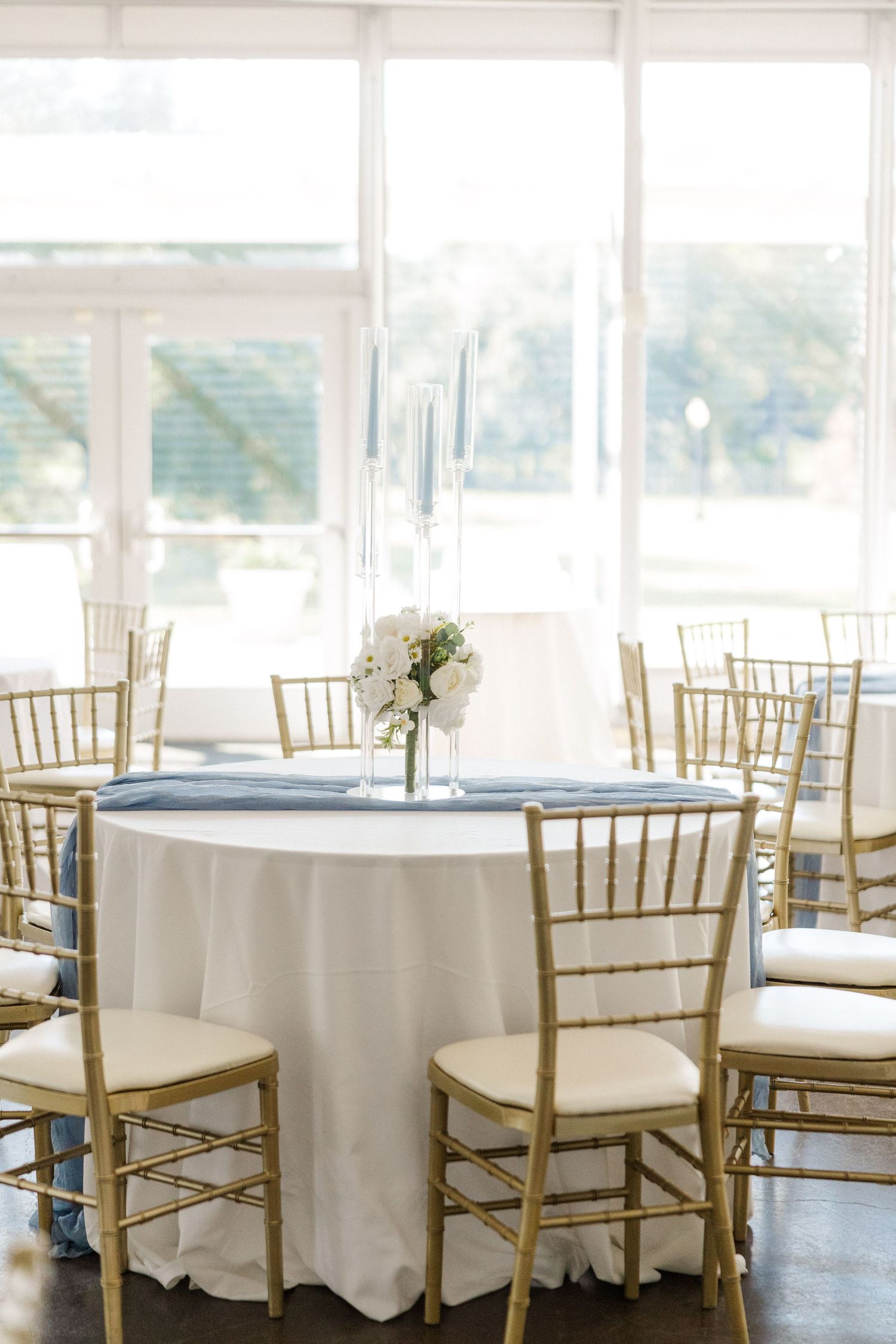 An elegant wedding reception venue with white tablecloths and gold chiavari chairs in a bright sunlit room.