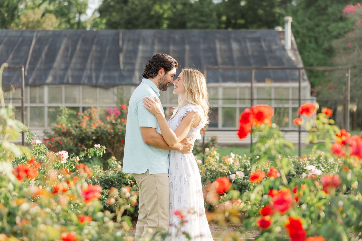 A romantic couple shares a tender moment in a vibrant garden filled with blooming red poppies and summer flowers.