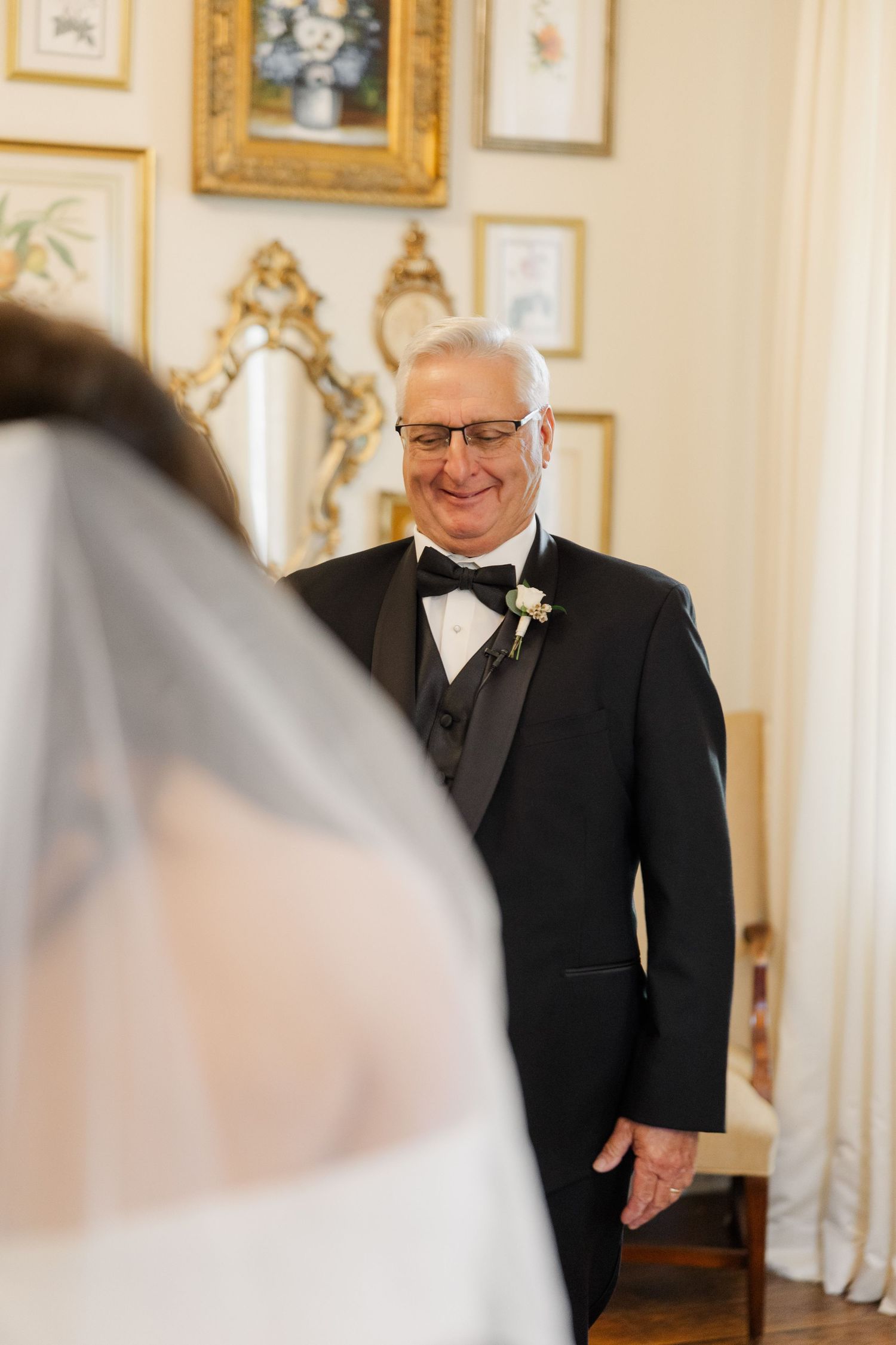 An emotional first look moment between a bride and her father in an elegant room with gold-framed artwork.