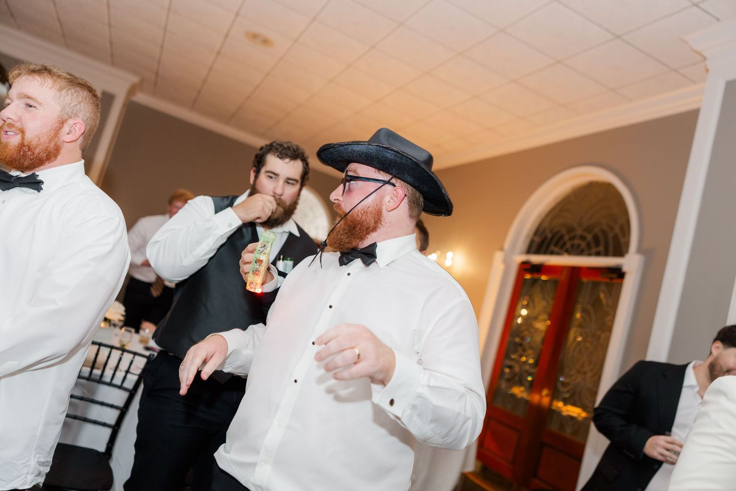 Wedding guests share laughter and drinks during a festive reception celebration.