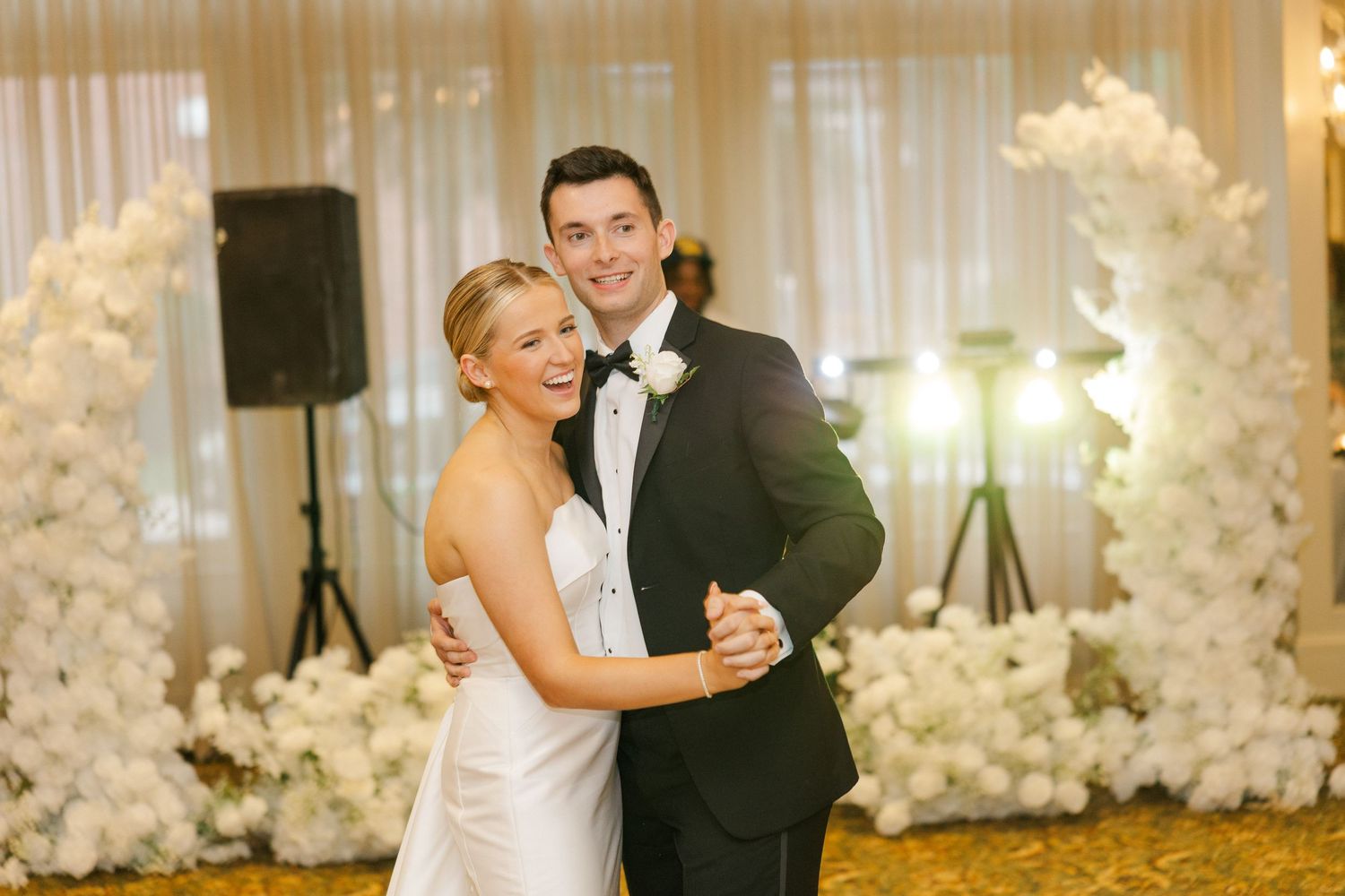 A couple shares their first dance as newlyweds surrounded by elegant white floral decorations.