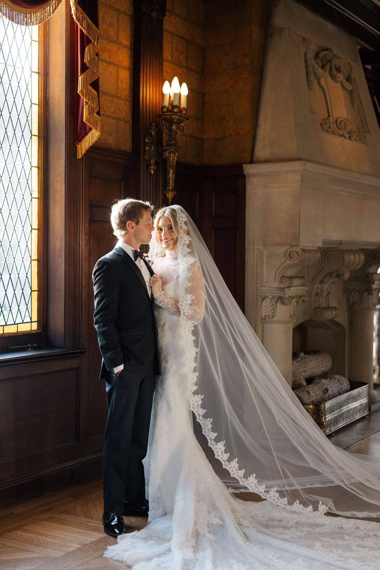 Wedding couple poses in a grand hallway with ornate architectural details and dramatic lighting.