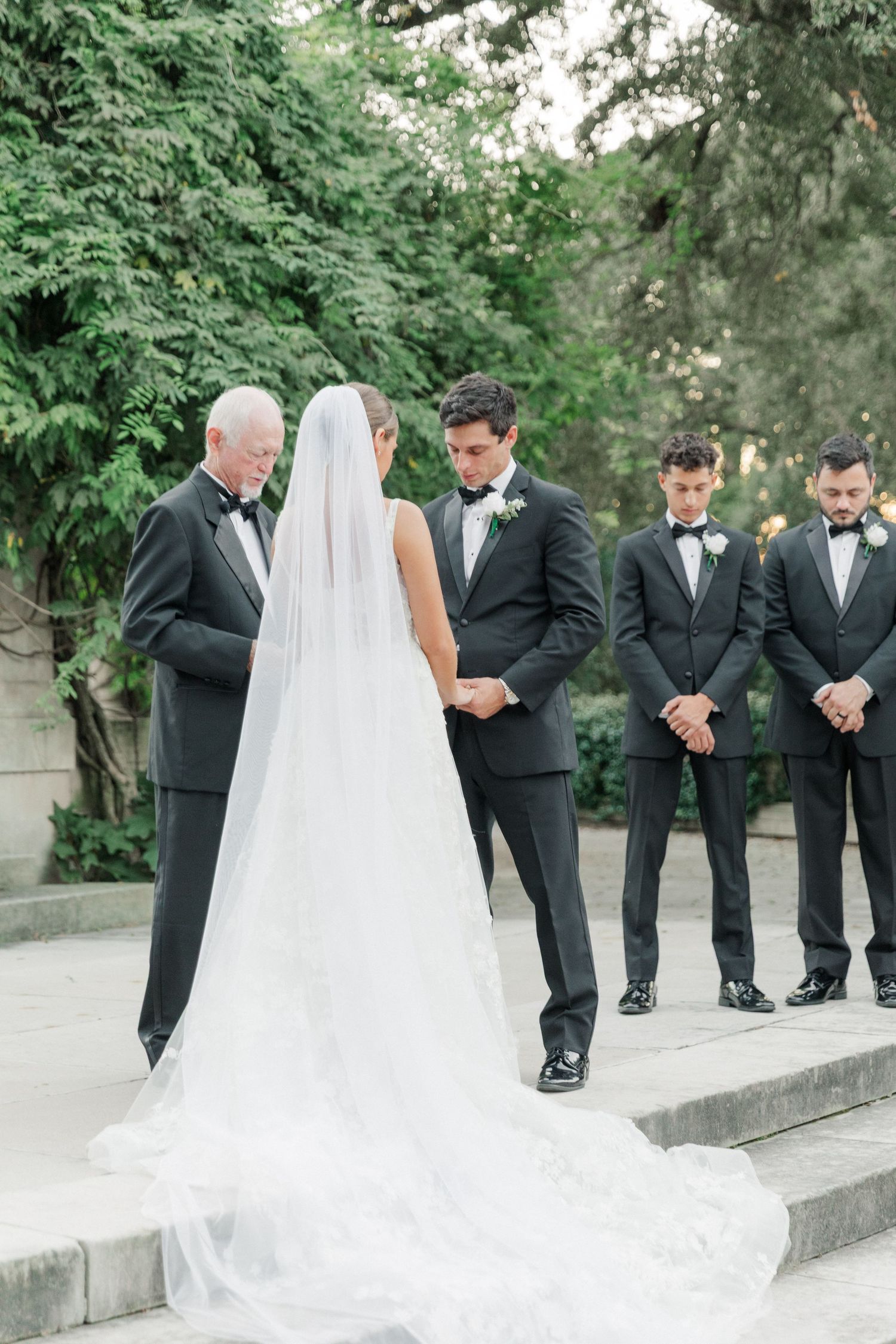 Wedding ceremony setup with groomsmen in black tuxedos and flowing white bridal veil.