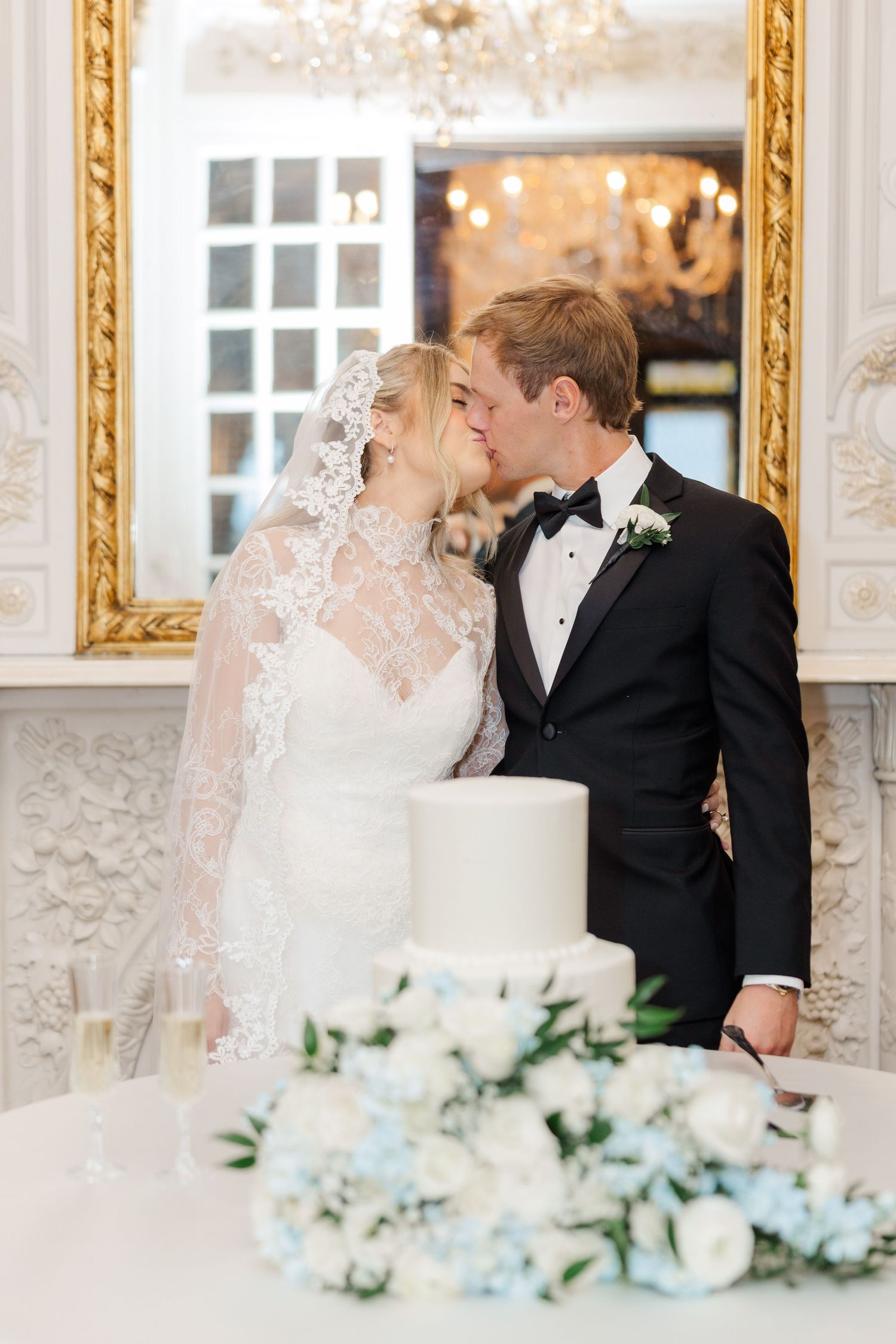 Elegant wedding scene with white cake and floral decorations in a gold-framed room.