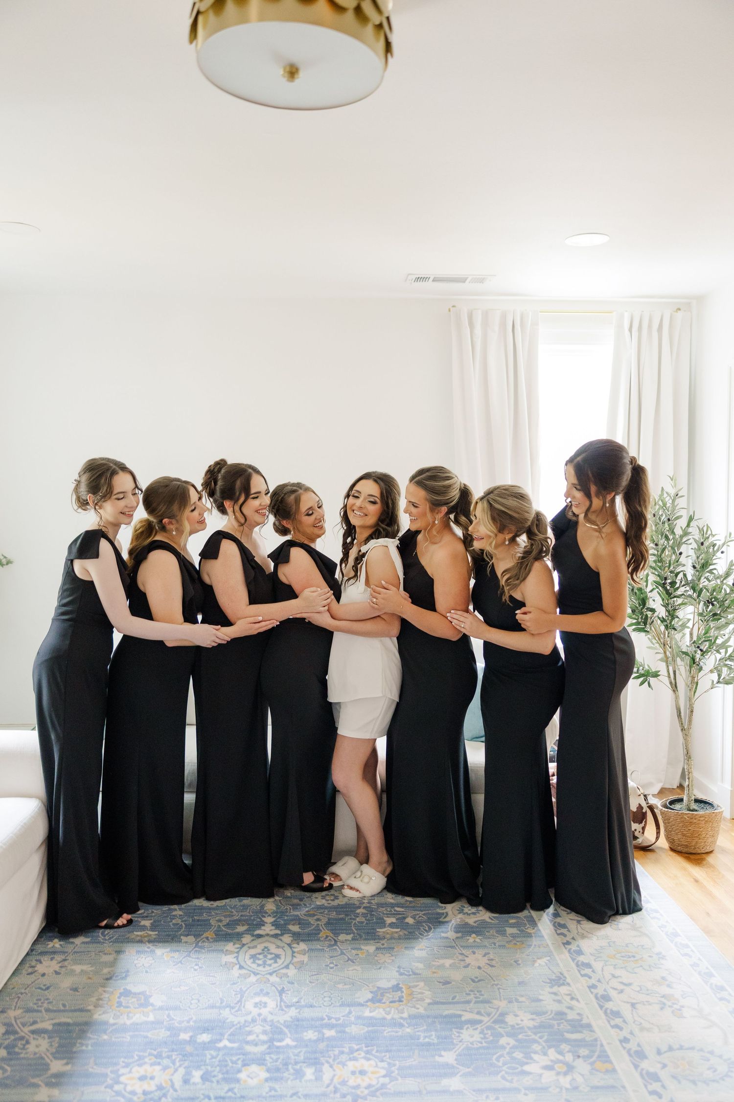 Bridesmaids in black dresses gather in a circle with the bride in white for a group photo.