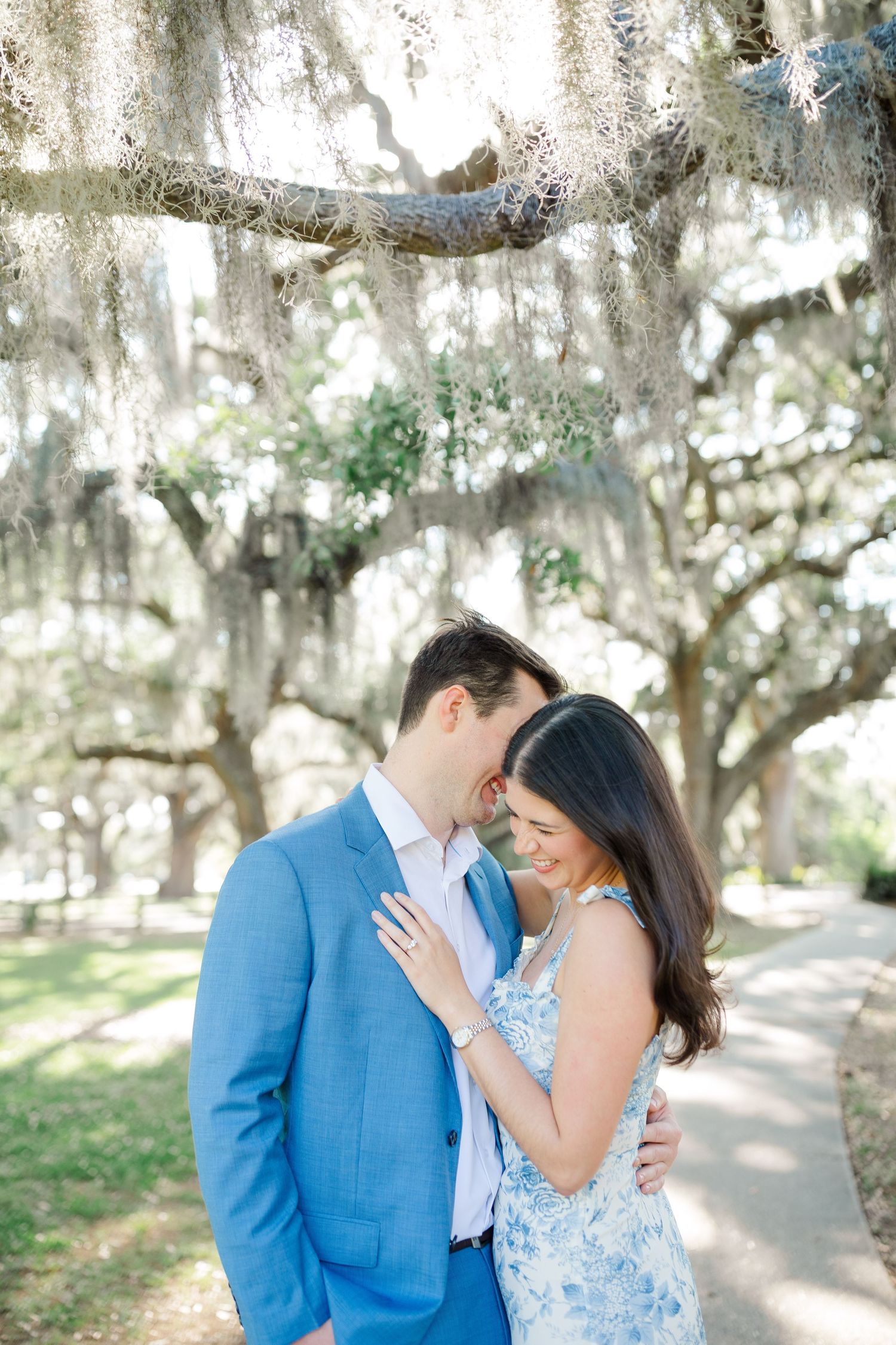 A romantic couple embraces under Spanish moss-draped oak trees on a sunny path.