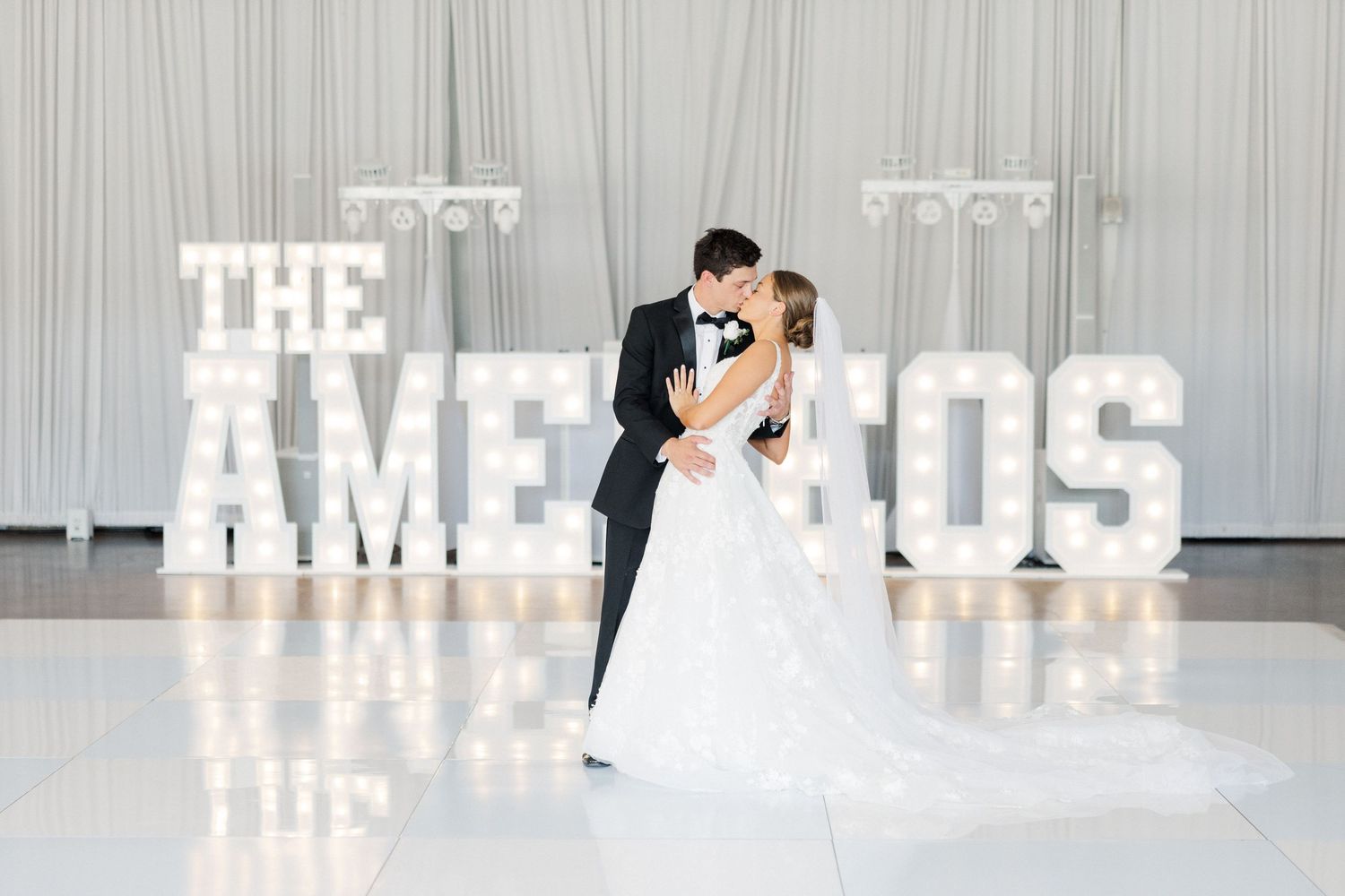 Wedding reception venue with illuminated marquee letters spelling a name against a white backdrop.