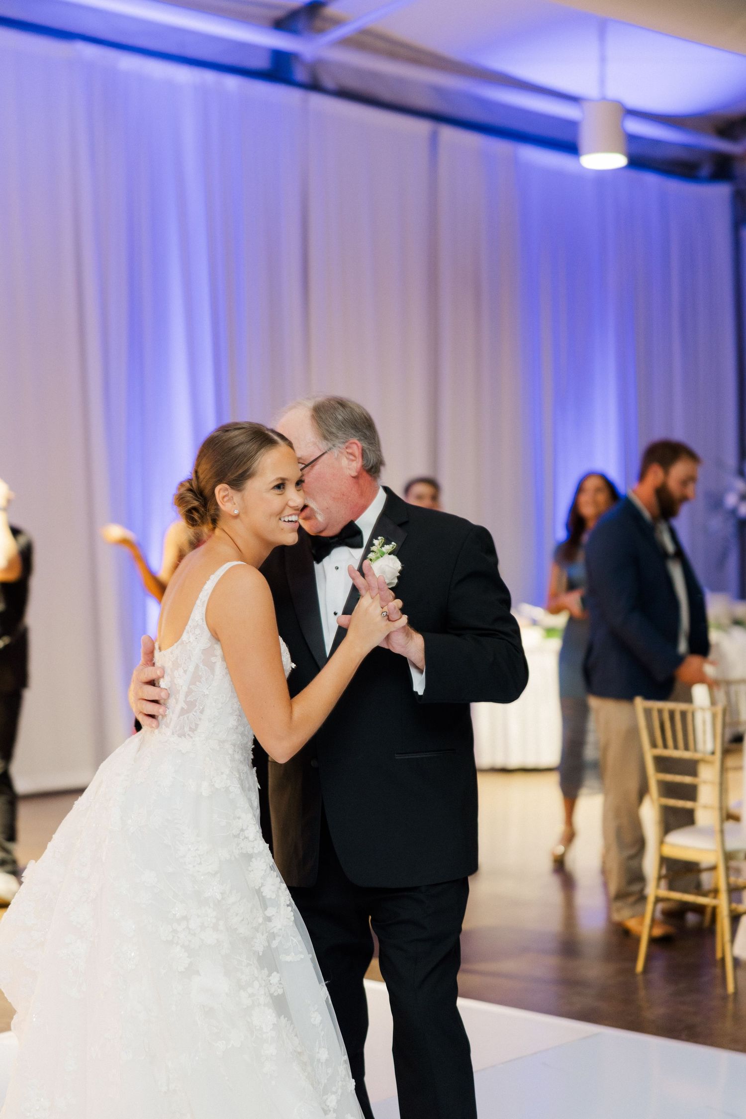 Bride and groom share a romantic dance together at their wedding reception with white drapes and blue lighting.