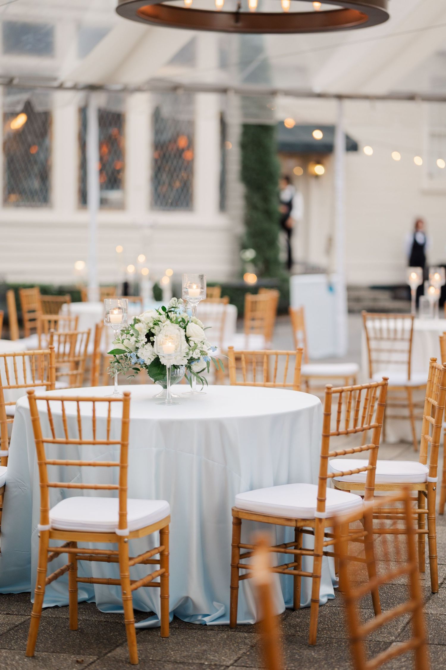 Wedding reception setup with chiavari chairs and pale blue linens under a white tent.