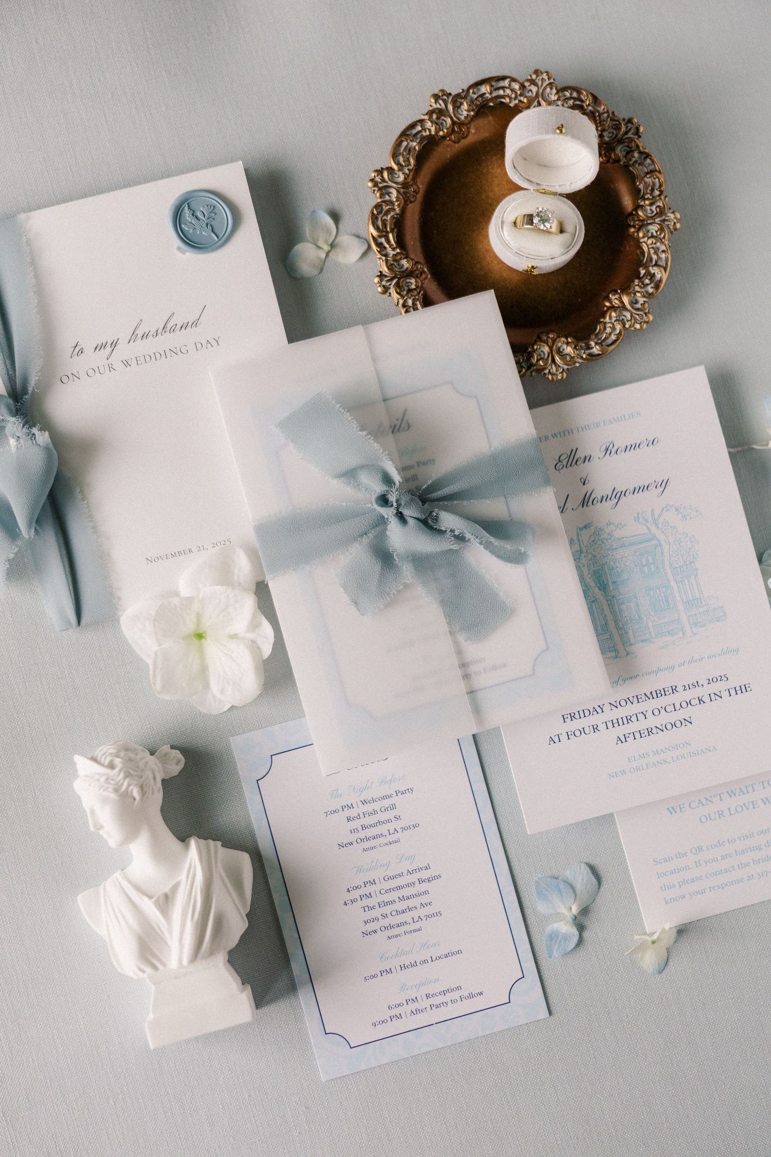 Elegant wedding invitations with light blue ribbons and white floral details on gray background.