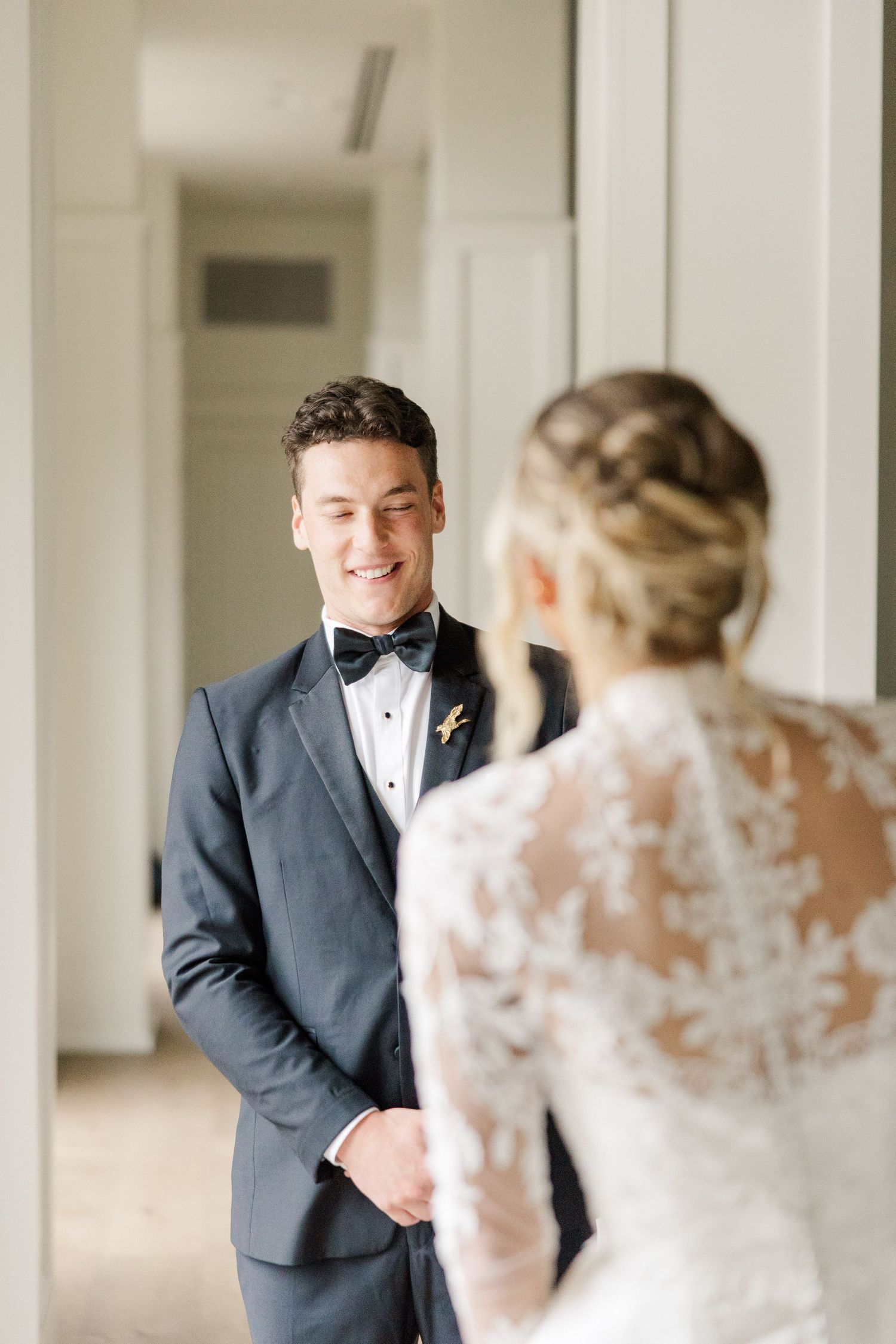 A wedding first look moment captured in an elegant white hallway with classic architectural details.