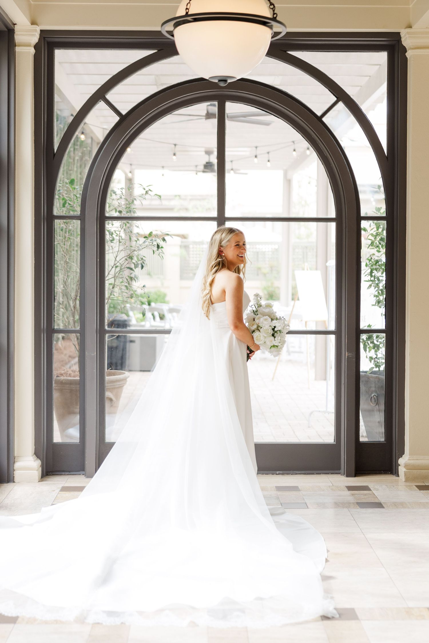 Elegant bridal portraits in front of arched windows and doors in a bright indoor venue.