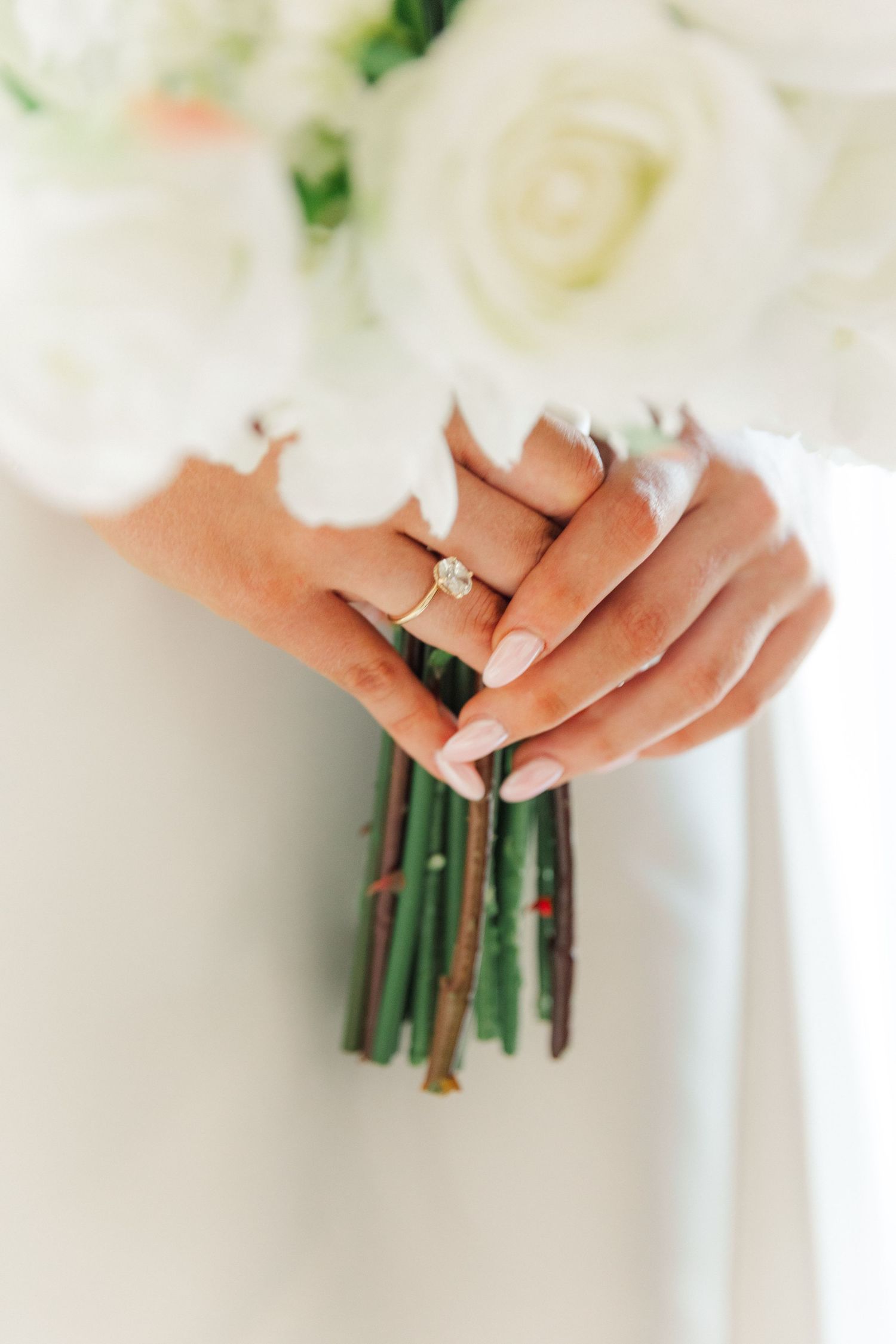 Close-up of hands holding a white floral wedding bouquet with green stems wrapped in ribbon.