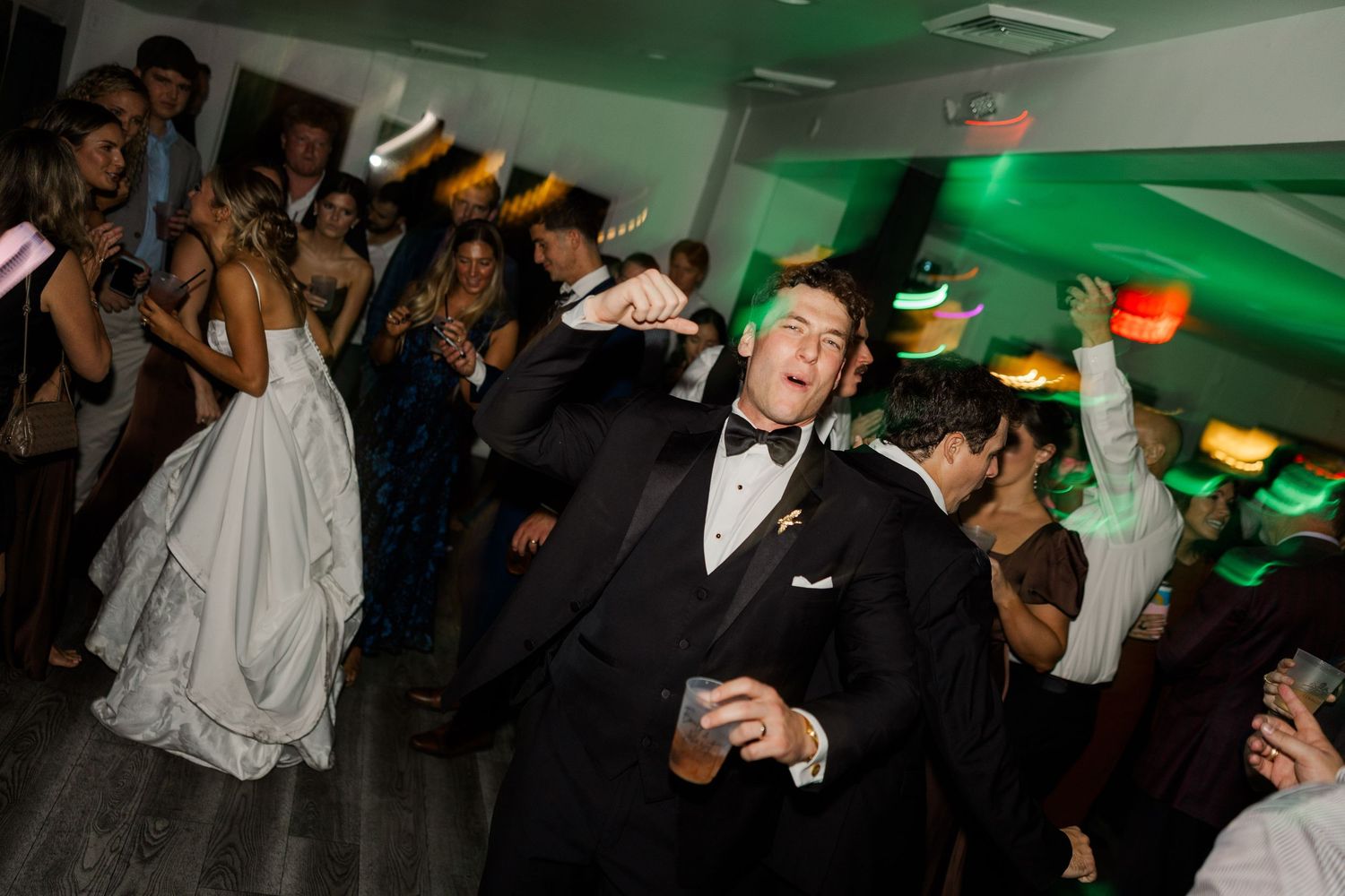 Wedding reception party scene with green lighting and guests dancing.