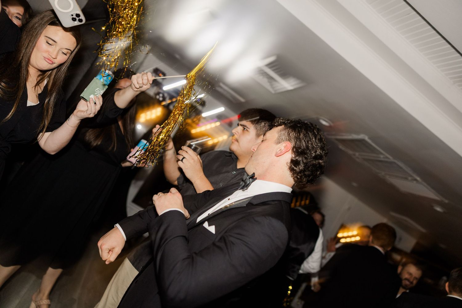 Wedding reception celebration with guests dancing under decorative lighting.