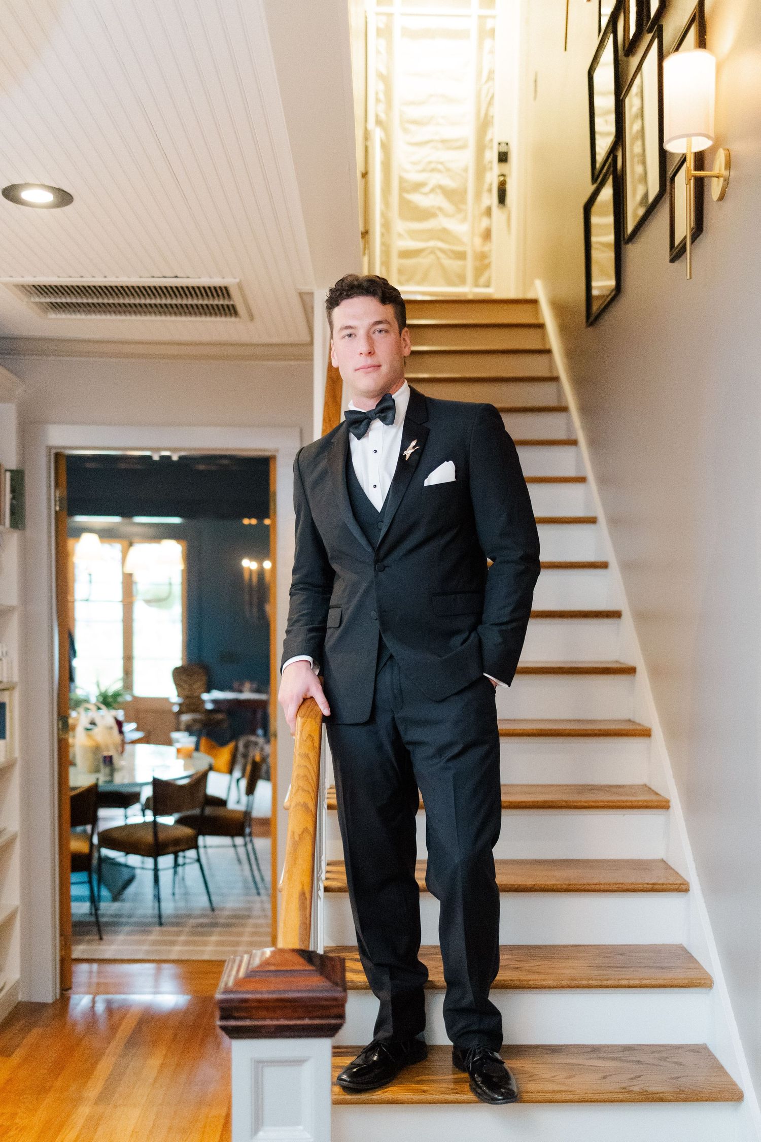 A formal black suit stands on wooden stairs in an elegant indoor setting.