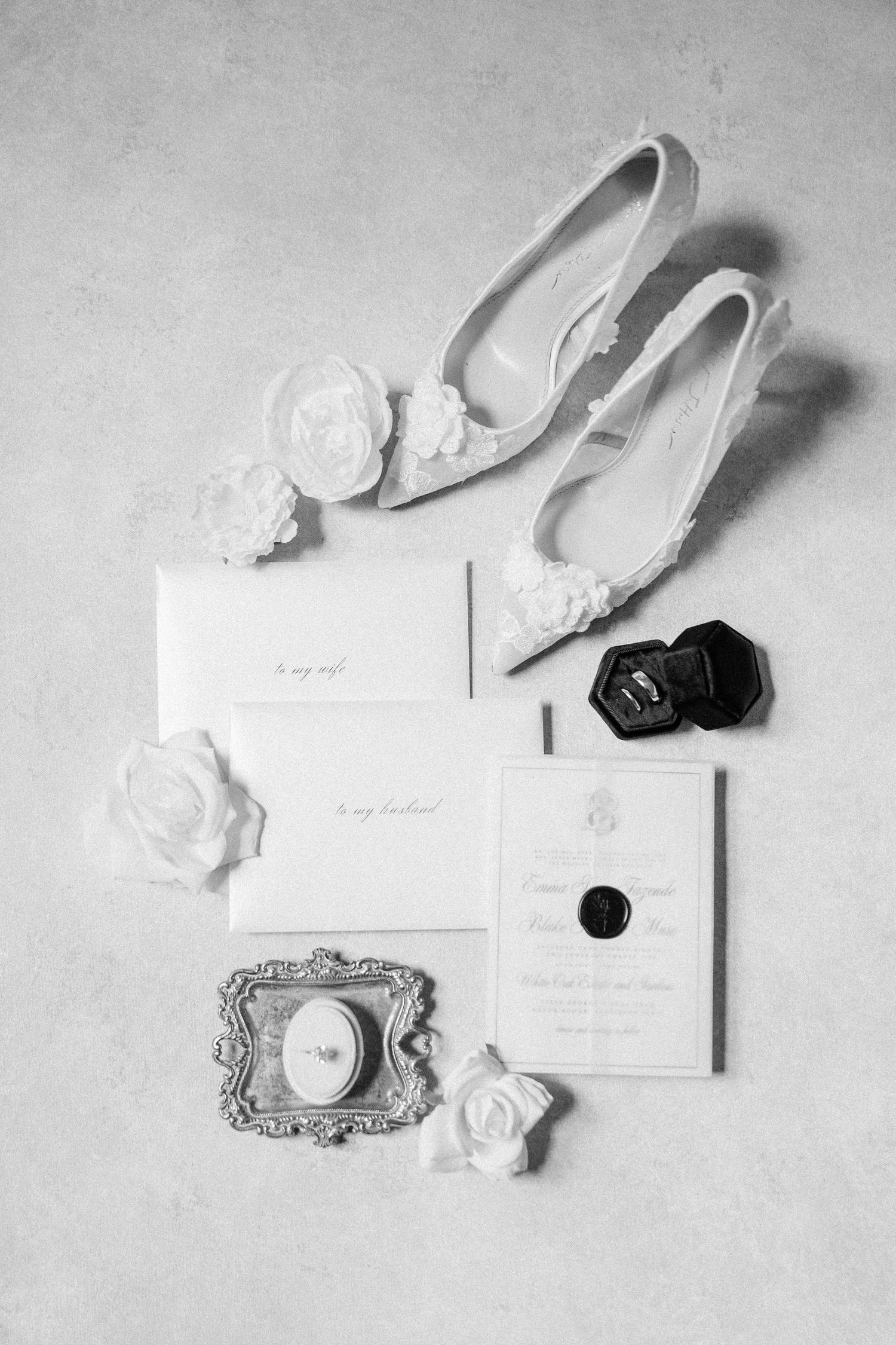 Black and white wedding details flatlay featuring invitations, flowers and bridal accessories.