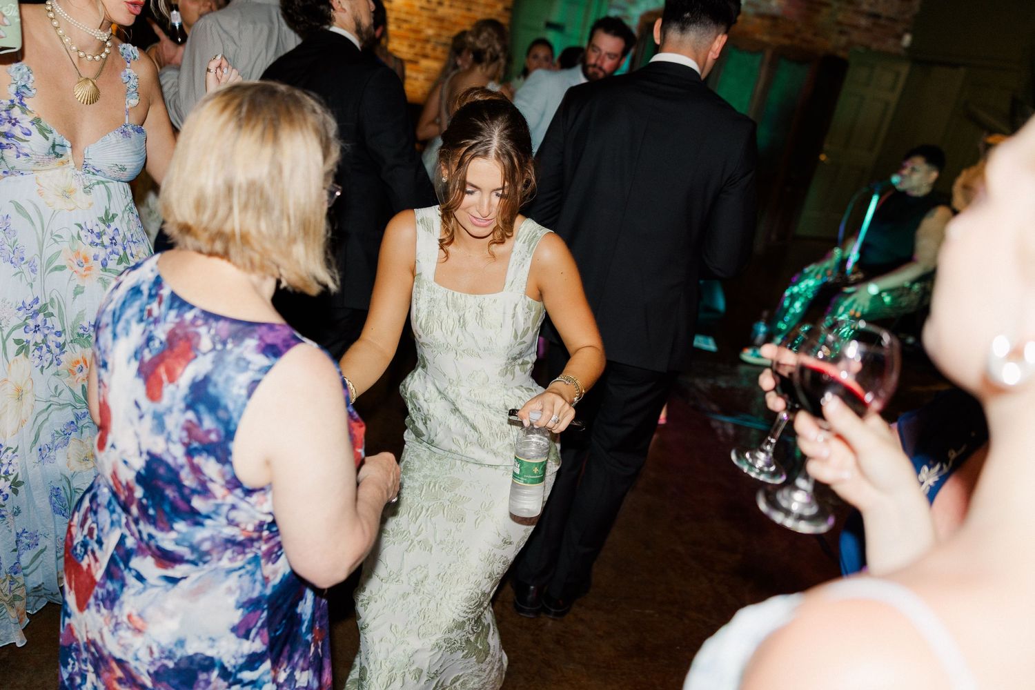 Guest in sage green dress dancing at lively wedding reception party.