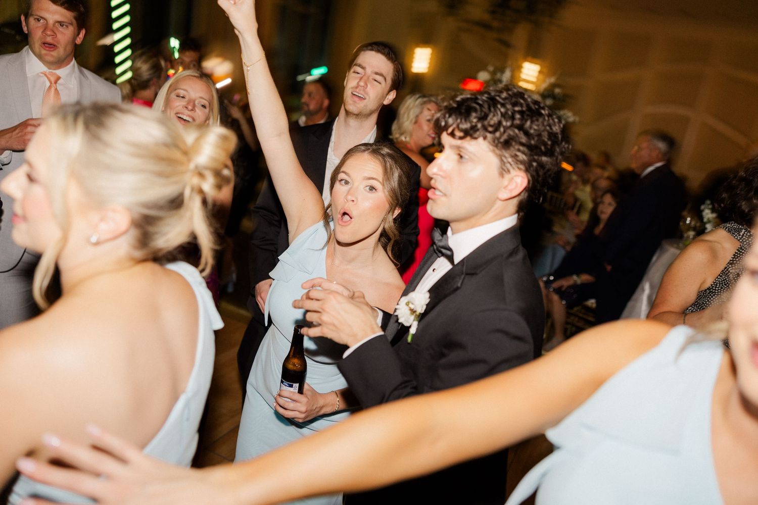 Excited wedding guests dance and celebrate energetically on the reception dance floor.