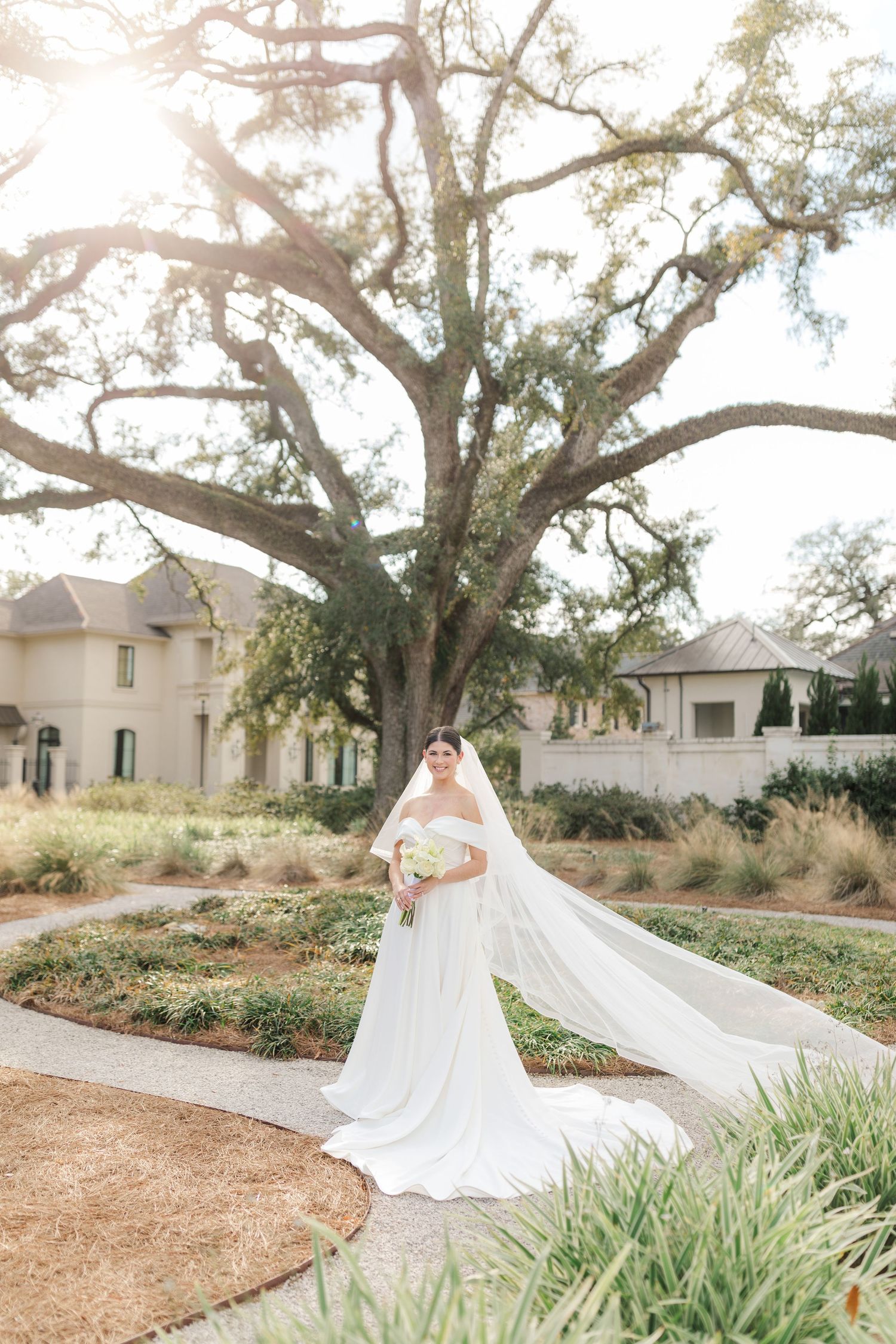 A long flowing white wedding dress with veil photographed in a garden setting beneath a majestic oak tree.