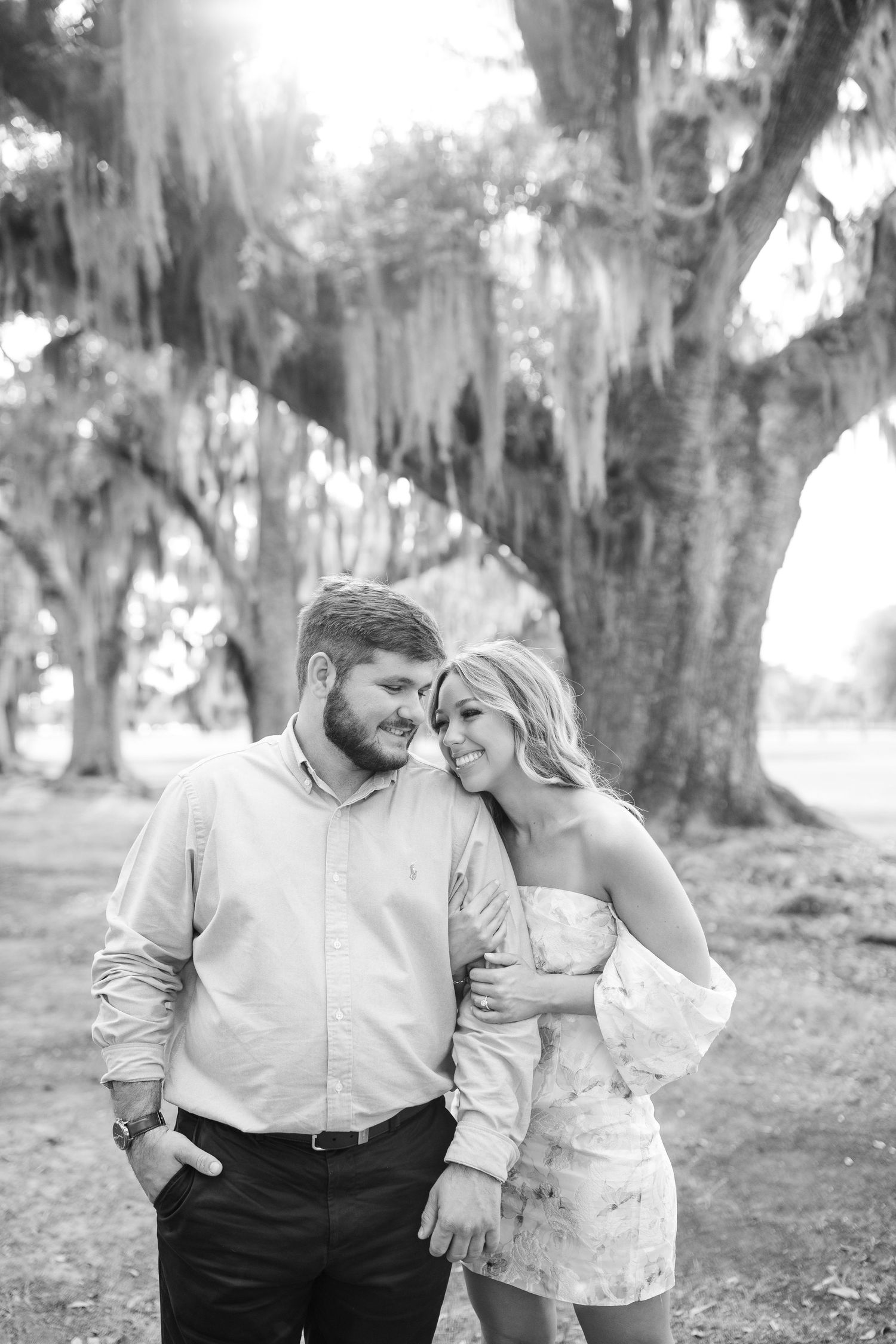 A black and white portrait of a couple sharing an intimate moment under oak trees with hanging moss.