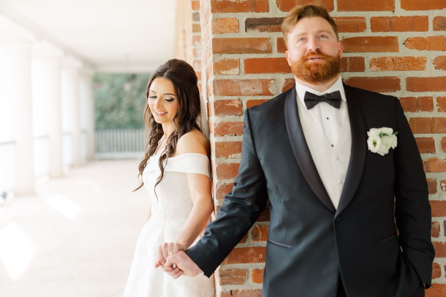 A couple poses together against a rustic brick wall in formal wedding attire.