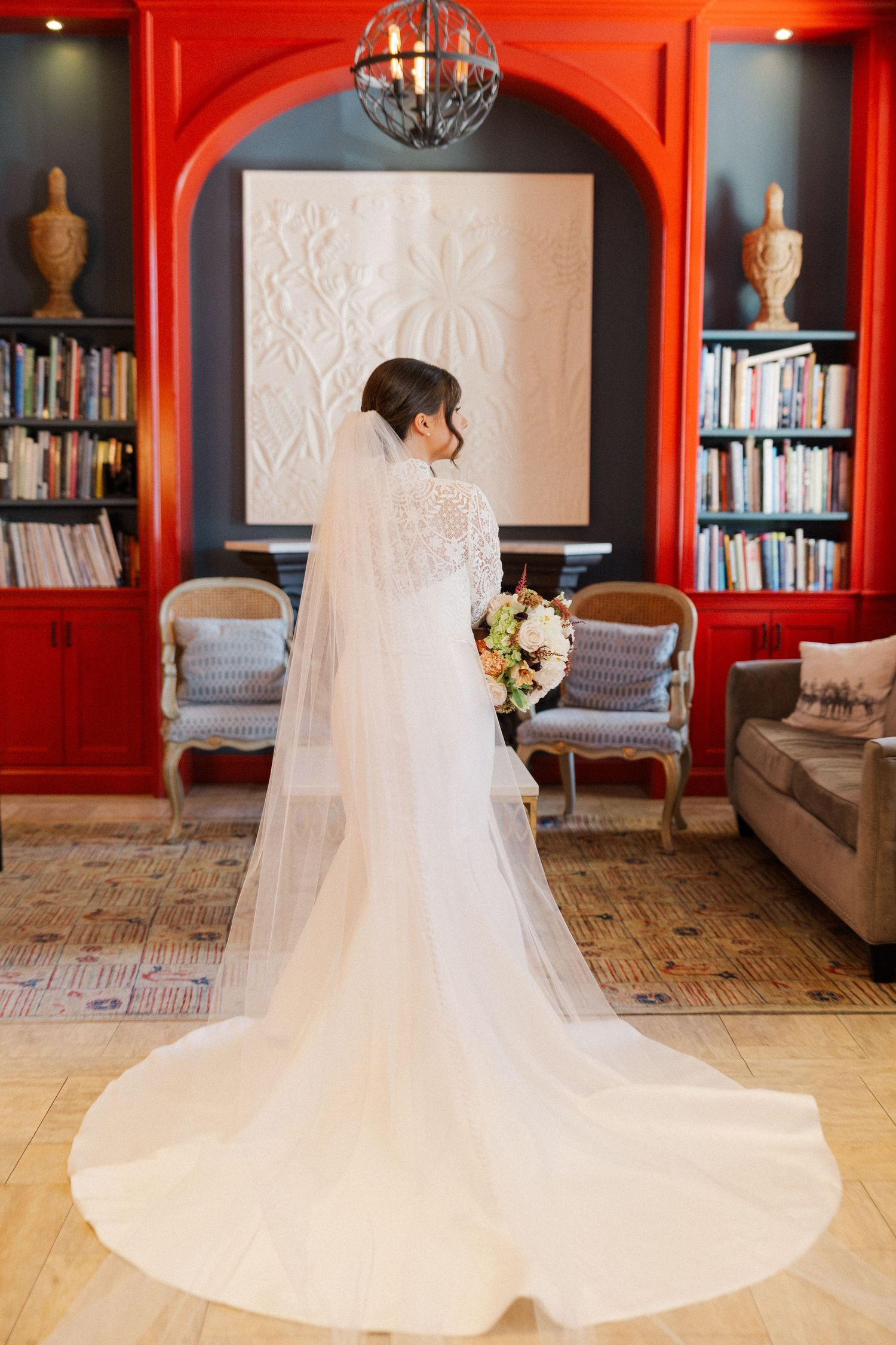Wedding dress with cathedral train photographed in a library with dramatic red walls and built-in bookshelves.