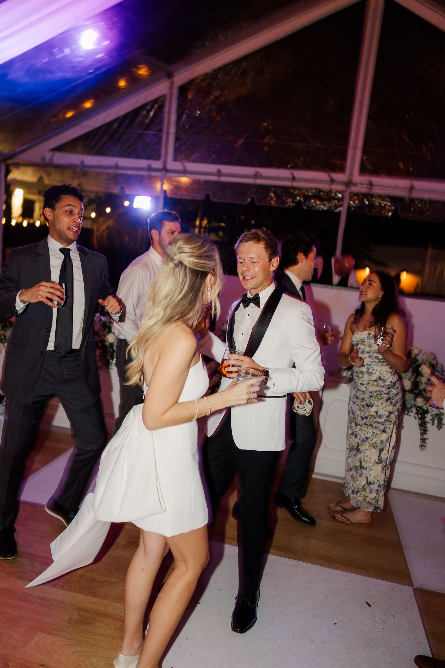 Wedding party dancing under purple and blue lighting at an evening reception.