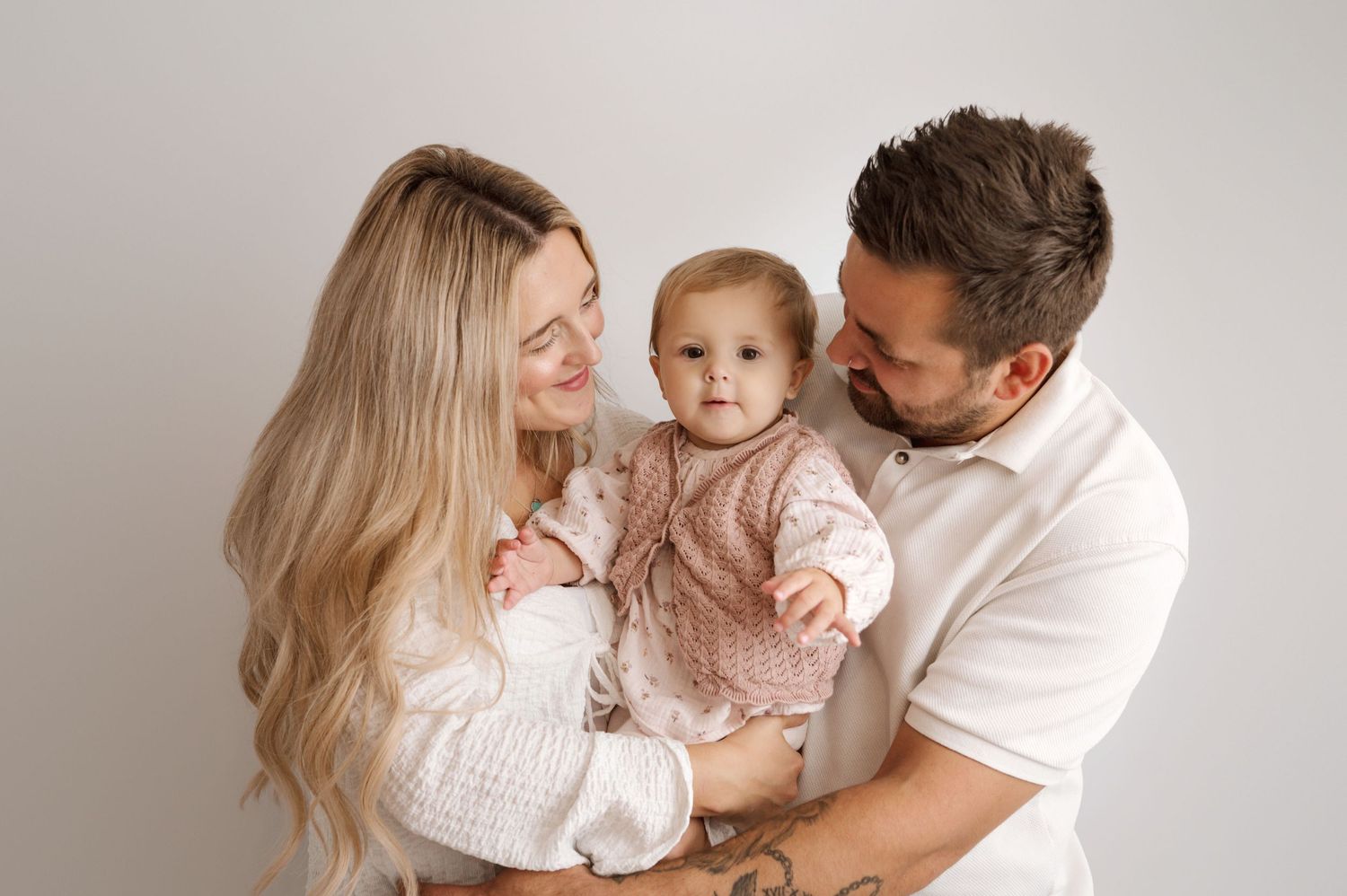 A family in white and pink outfits poses together against a light gray backdrop for a studio portrait.