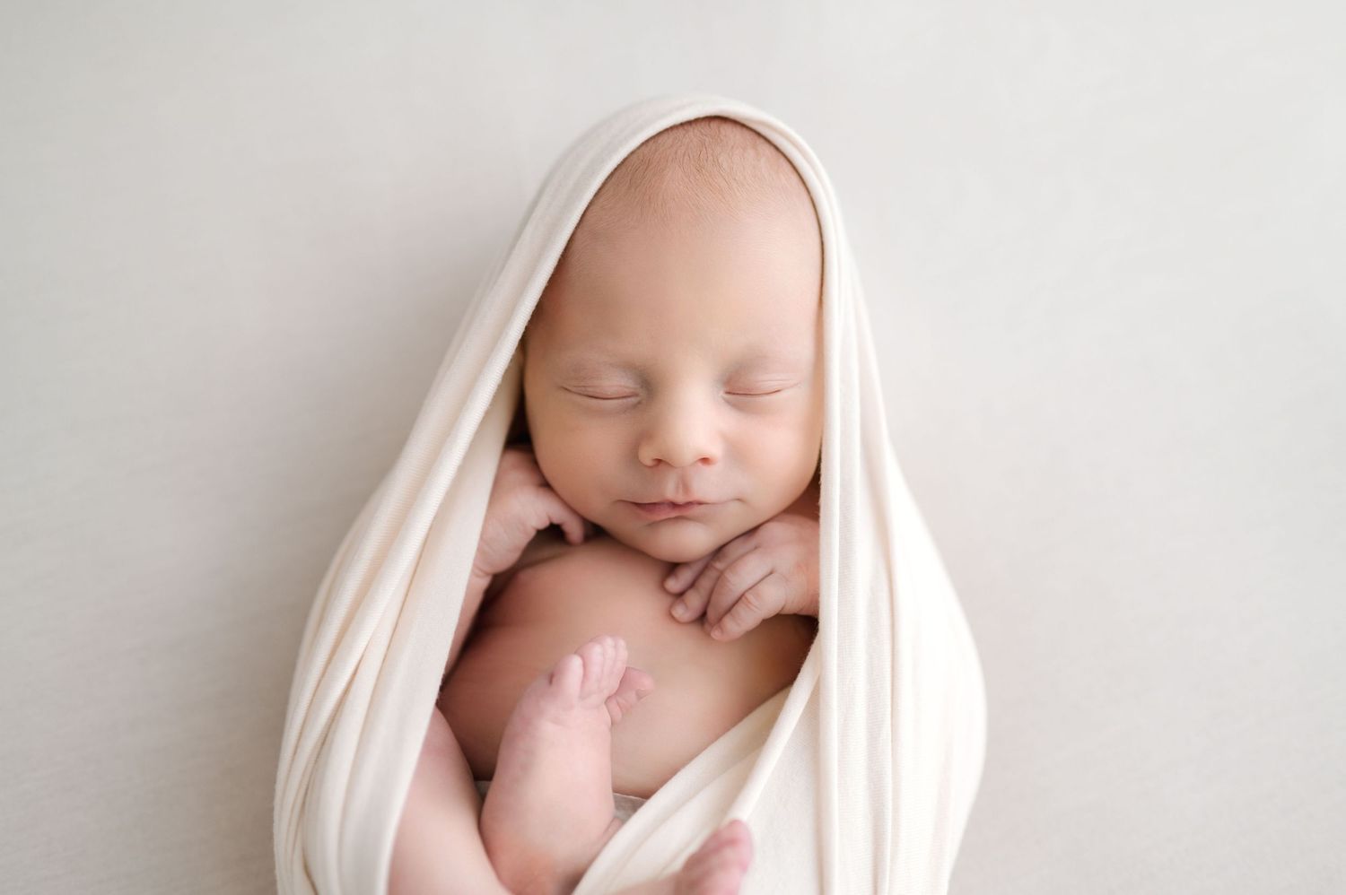 Peaceful newborn baby sleeping wrapped in soft cream white swaddle blanket in professional studio photo.