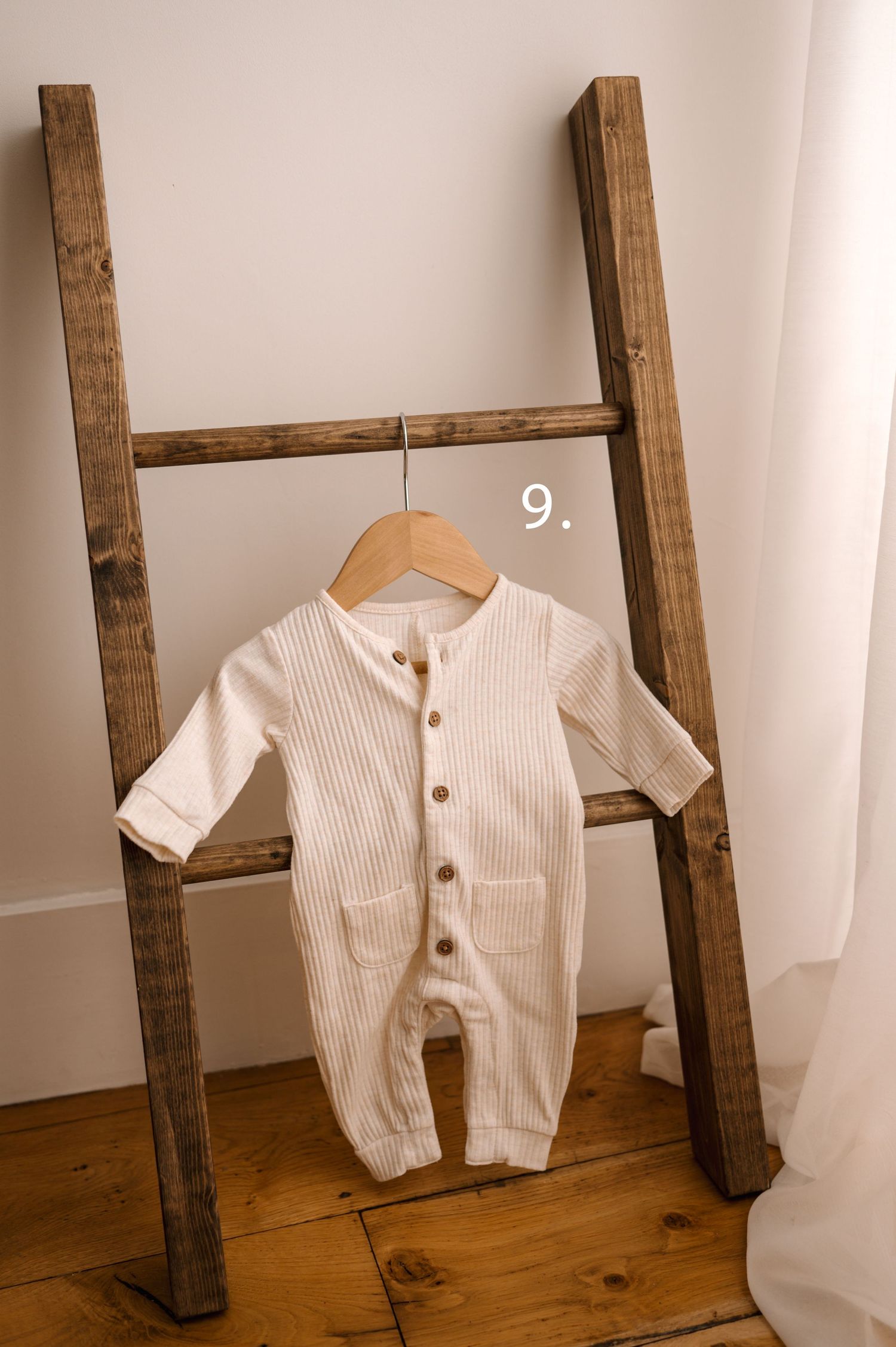 White ribbed baby romper with wooden buttons displayed on rustic wooden ladder against white wall.