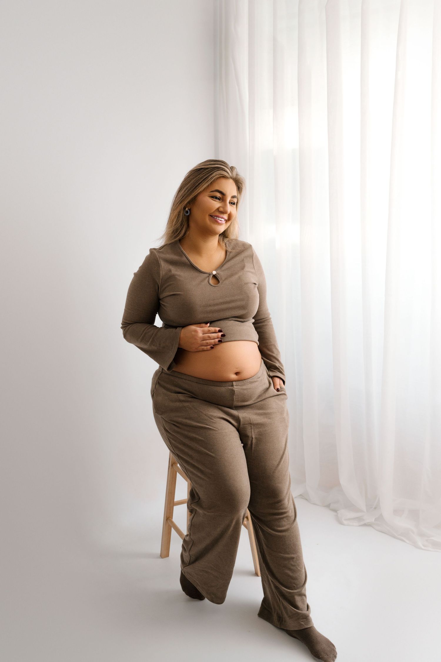 A plus size model in brown loungewear poses confidently against a white backdrop in a studio setting.