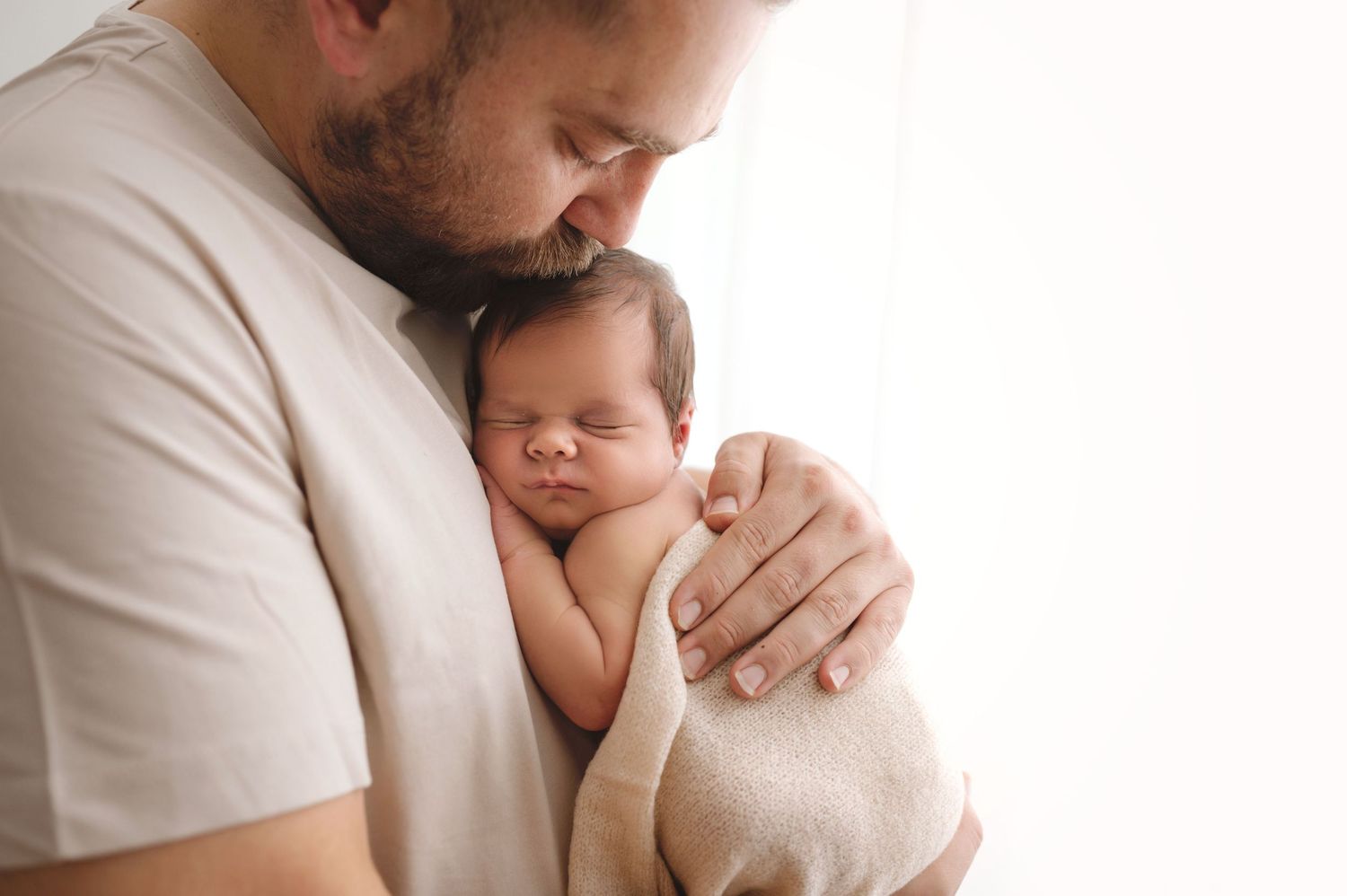 A tender moment captured in soft light as a newborn baby sleeps peacefully on his father.