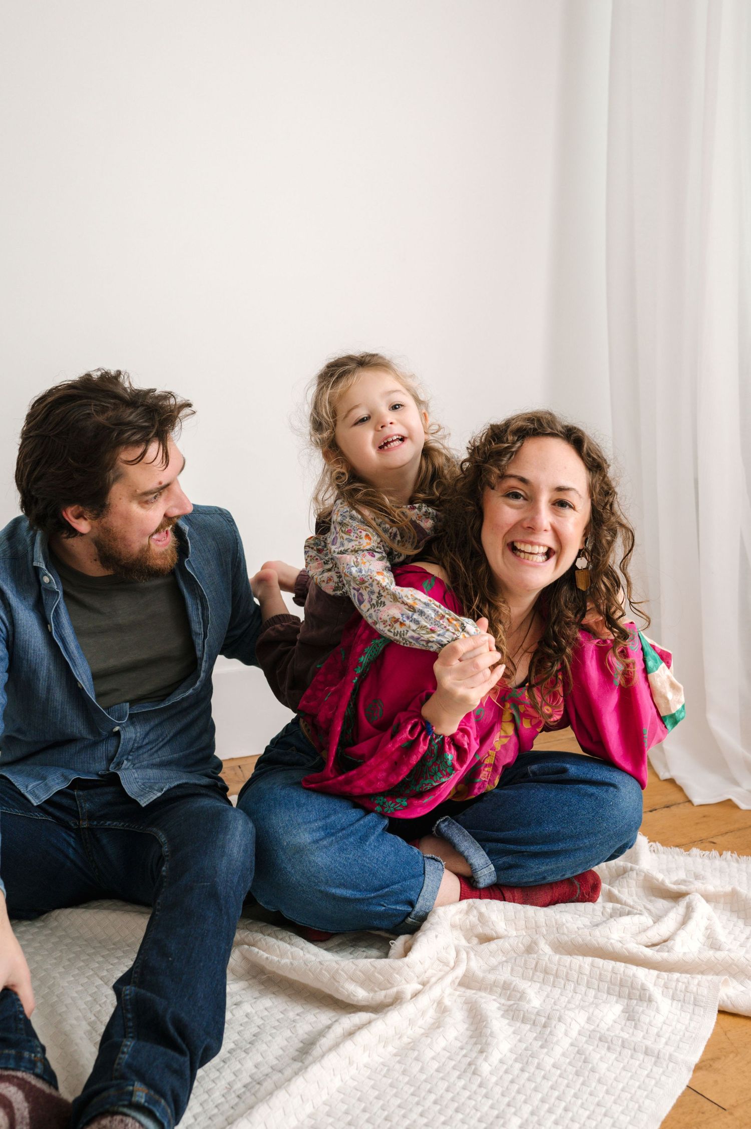 A series of playful candid moments between family members relaxing on a white blanket.